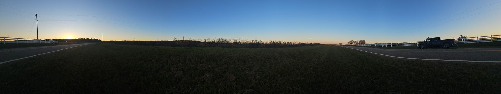 Panoramic view of a field, road, and buildings under a blue and golden sky.
