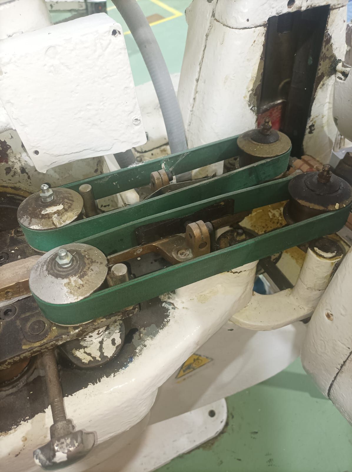 Brazos de conexión y pernos de metal verde en un conjunto de máquina blanca con un cable negro.