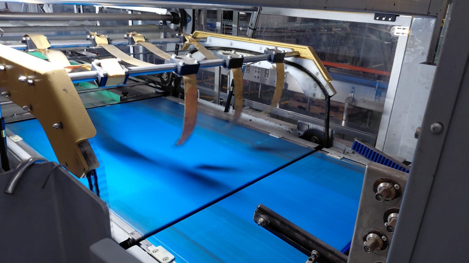 Máquina industrial que manipula material azul en una línea transportadora de fábrica.