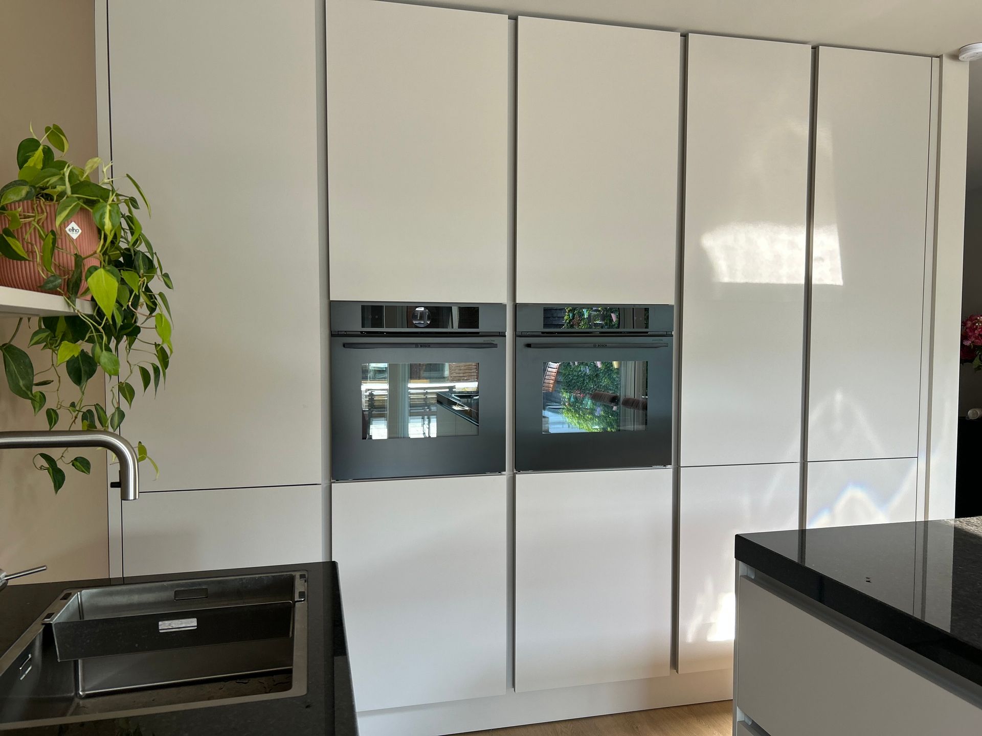 Moderne keuken met witte kasten, kookeiland, ingebouwde oven en koffiezetapparaat langs de muur.