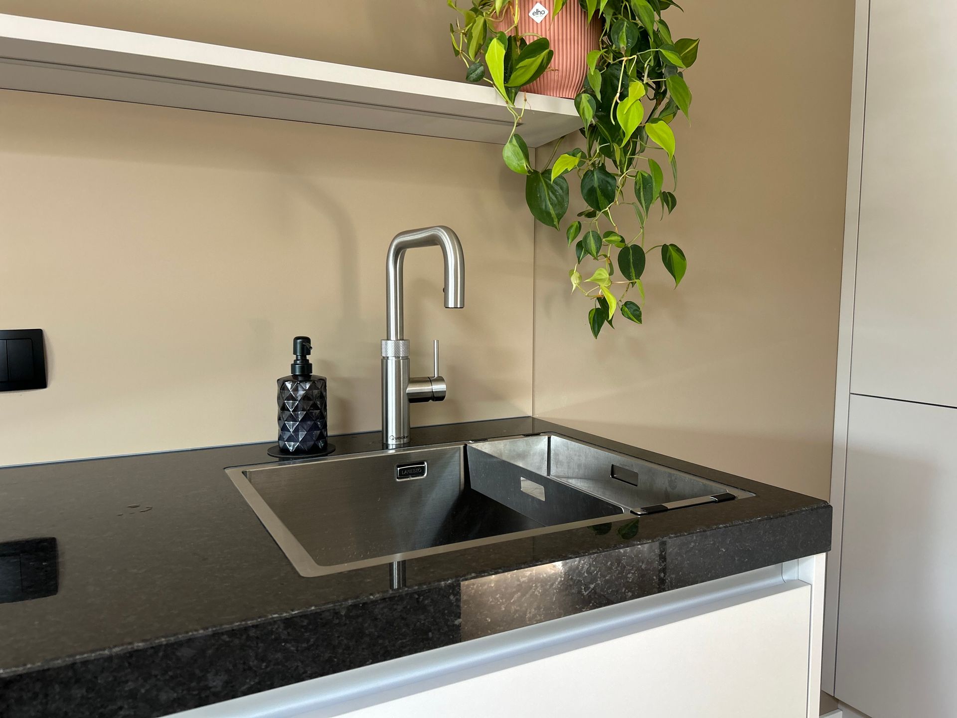Een vaas met paarse bloemen op een keukeneiland naast een klein kaarsje, met een moderne keuken op de achtergrond.