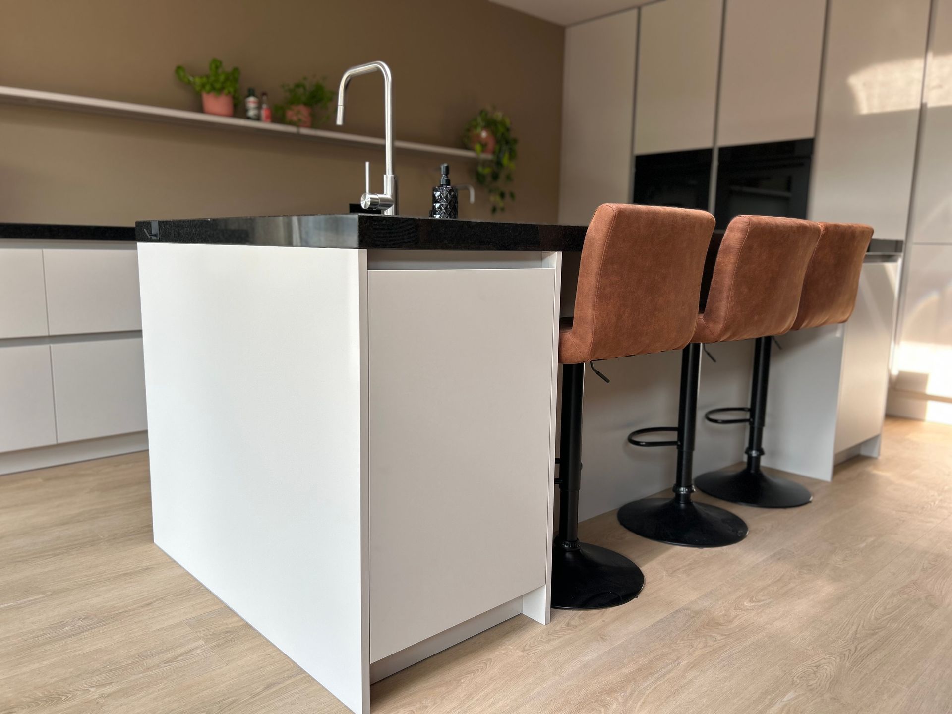 Modern keukeneiland met licht aanrechtblad, vaas als middelpunt en warme houten vloer.