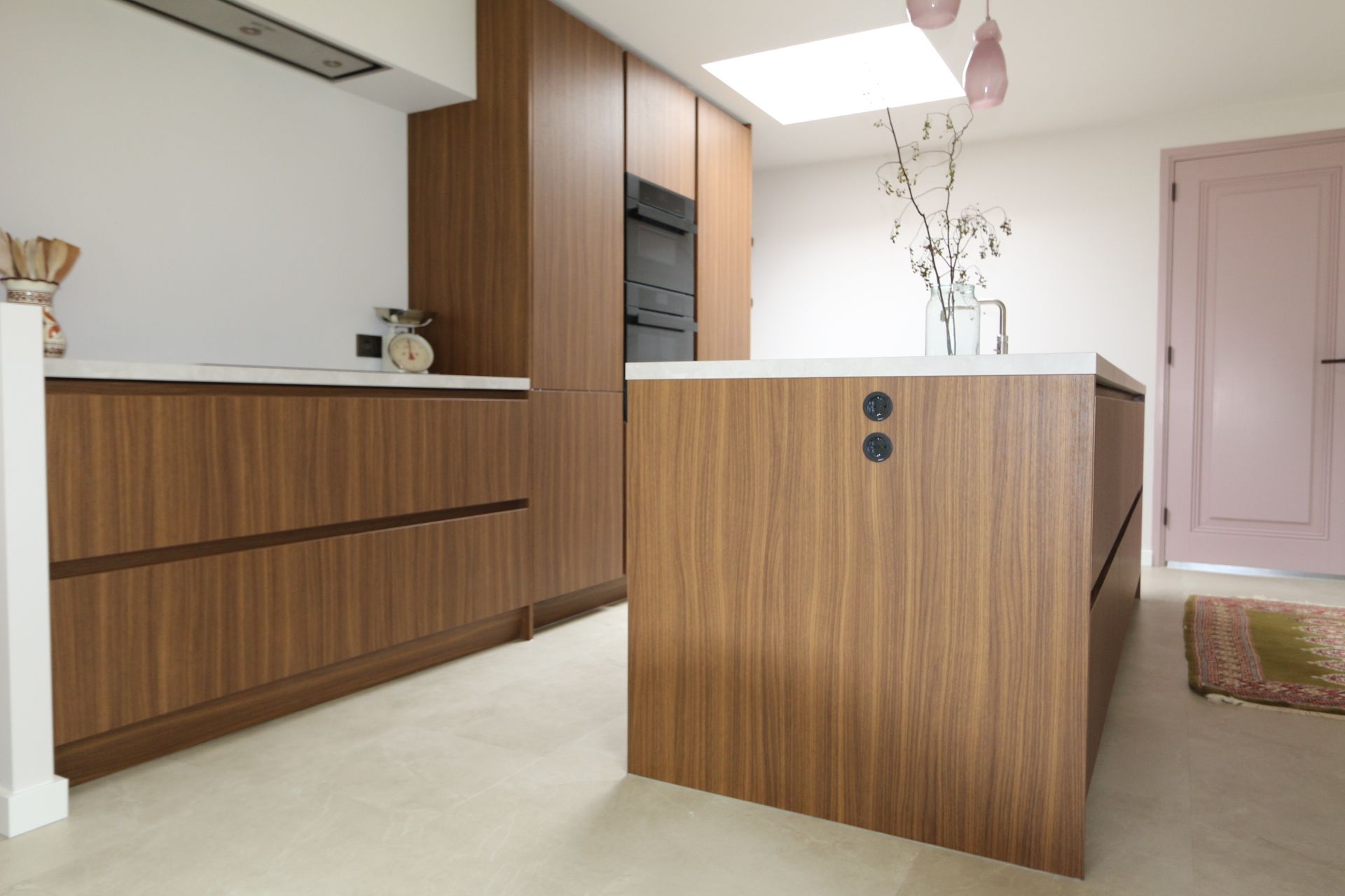 Moderne keuken met wit kookeiland, zwart aanrechtblad en ingebouwde apparatuur in een minimalistische ruimte.