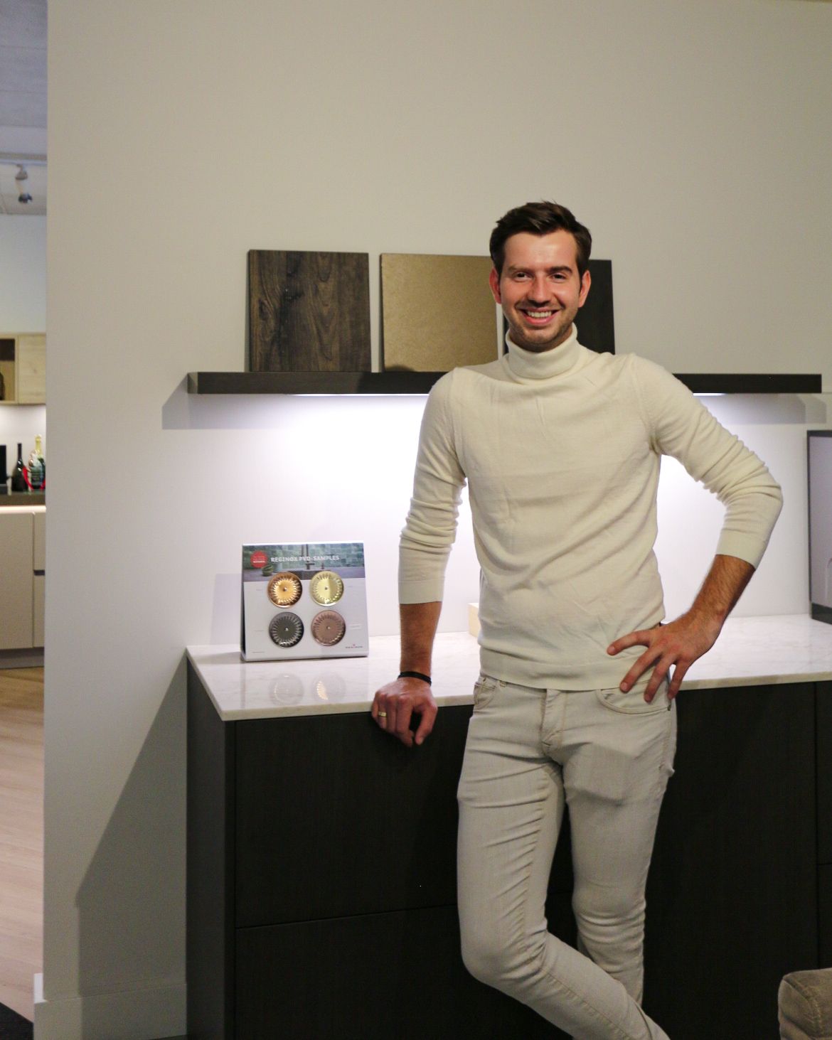 Twee mannen staan in een moderne keuken, de ene glimlachend met de armen over elkaar, de andere in een blazer en spijkerbroek.