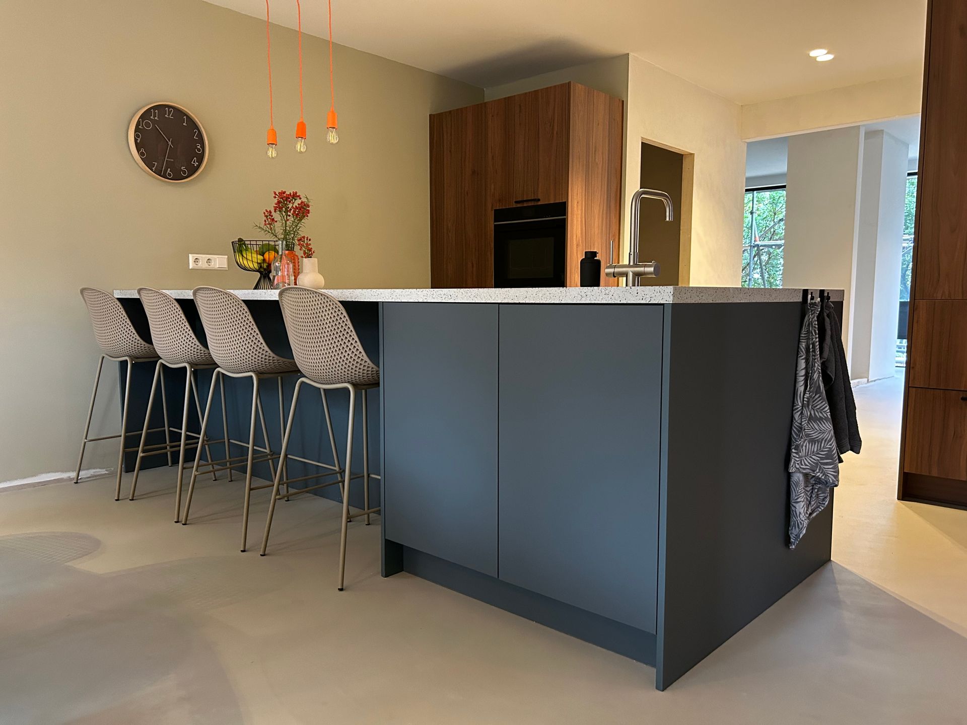 Moderne keuken met grijs kookeiland, barkrukken, hanglampen en houten keukenkasten.