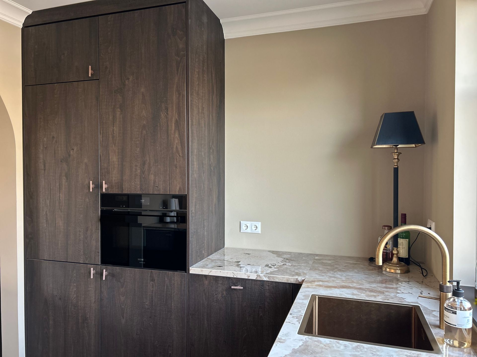 Moderne keuken met donkerhouten kasten, granieten aanrechtblad, spoelbak en staande lamp bij een beige muur.