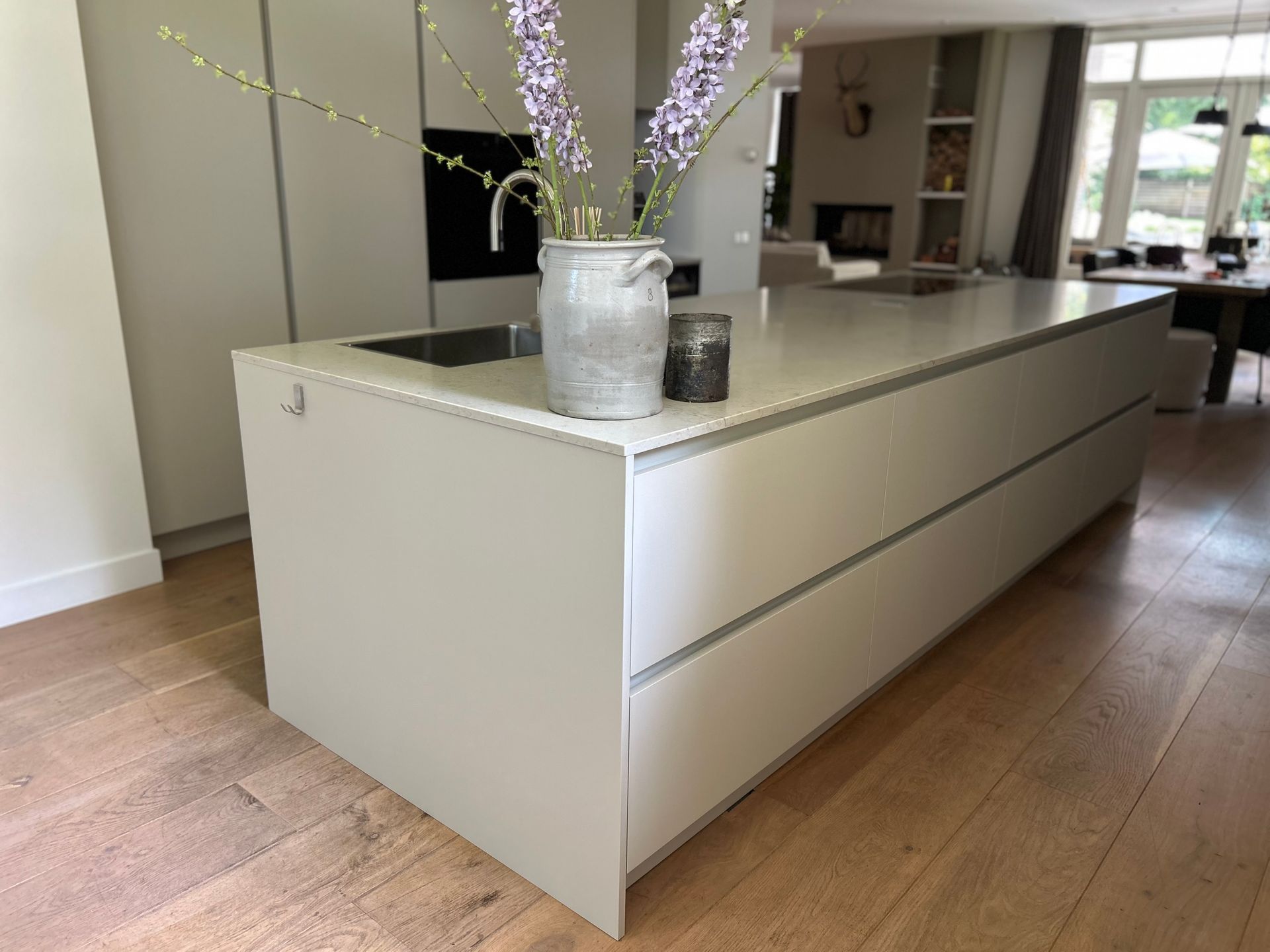 Modern keukeneiland met licht aanrechtblad, vaas als middelpunt en warme houten vloer.
