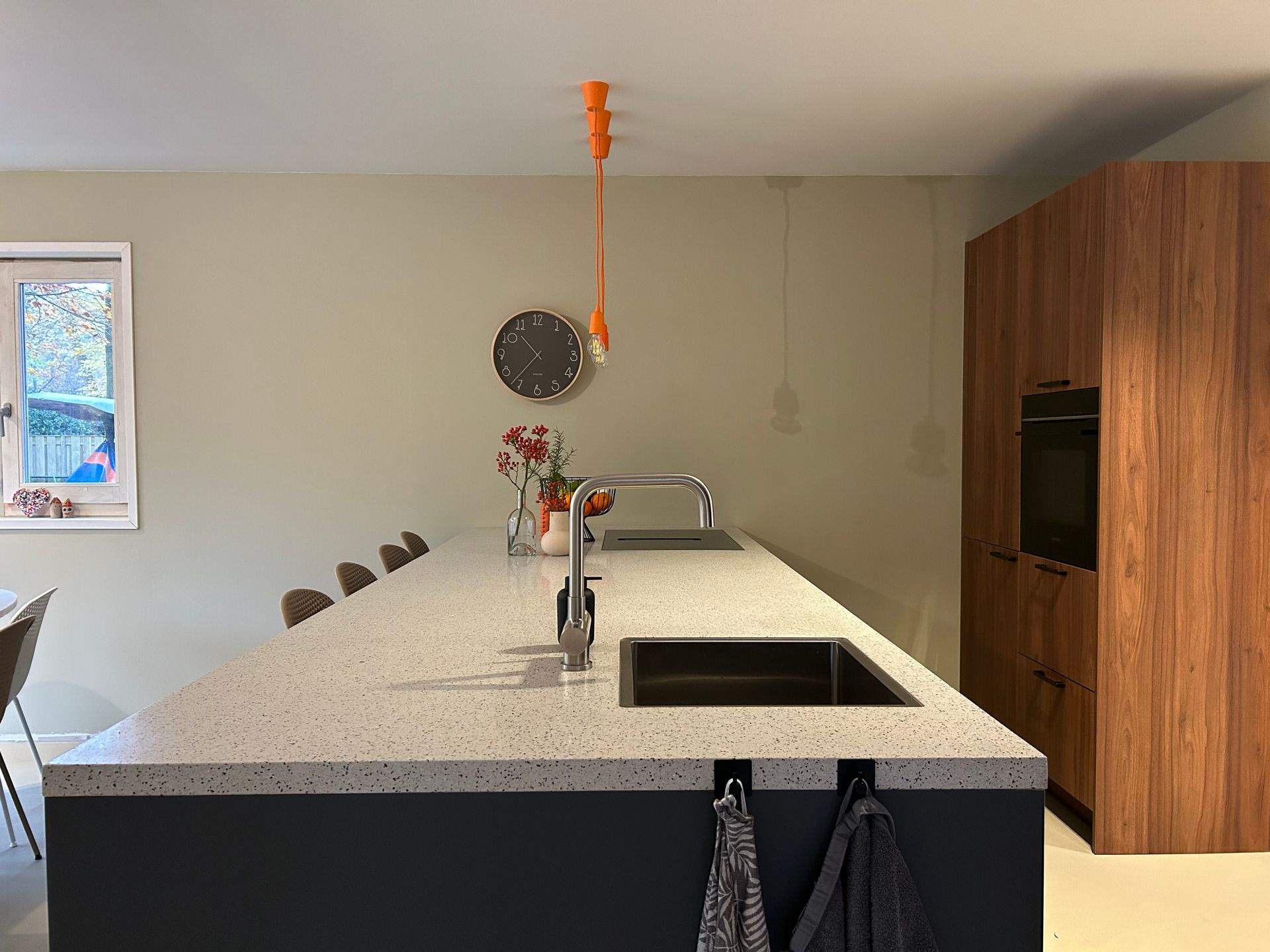 Moderne keuken met wit kookeiland, spoelbak, barkrukken en houten kasten bij een raam.