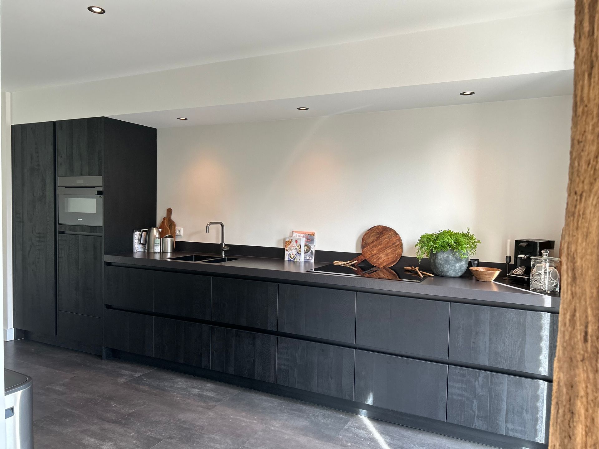 Moderne keuken met zwarte kasten, een lang aanrechtblad en decoratieve elementen tegen witte muren.