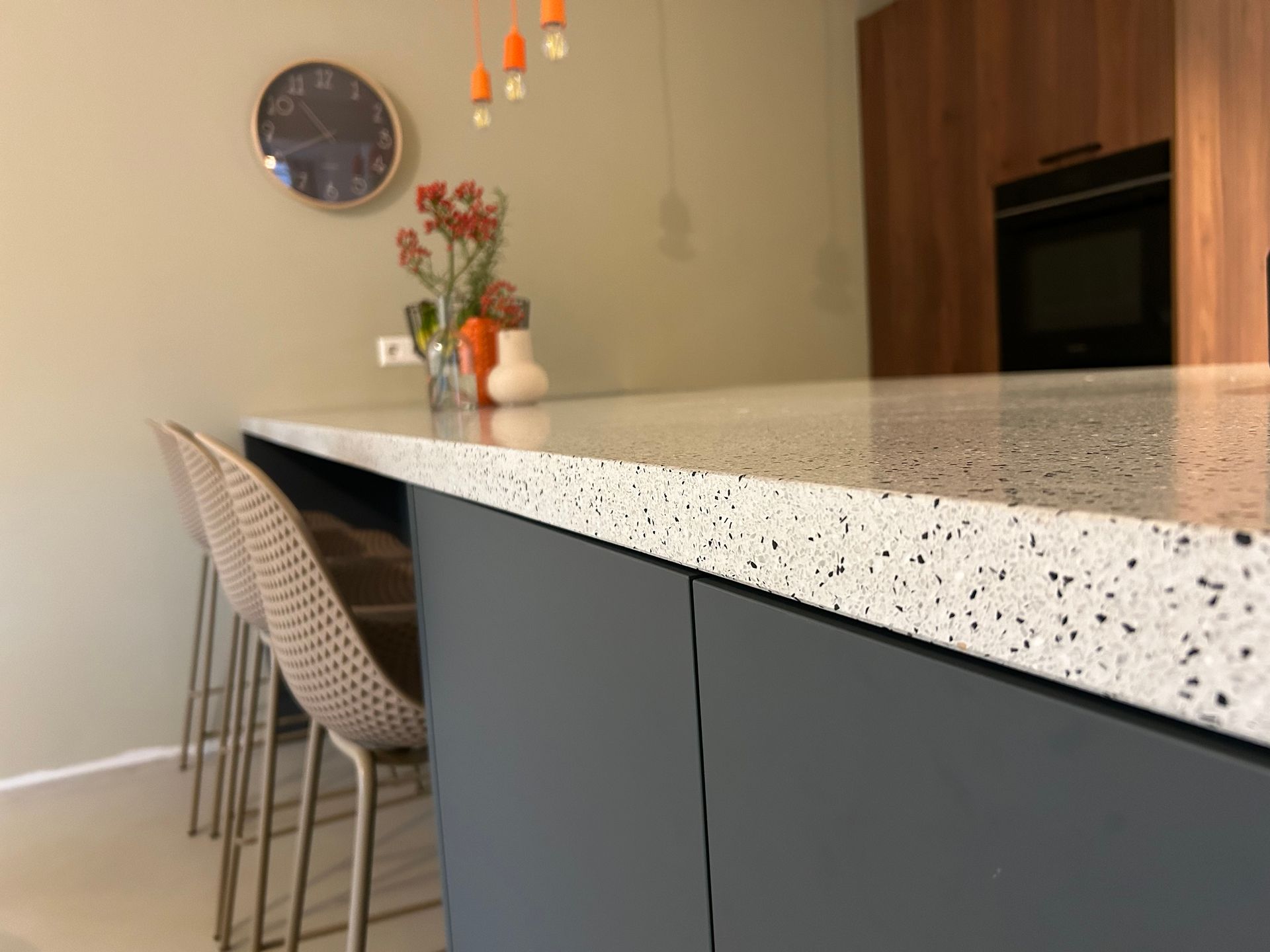 Moderne keuken met gespikkeld aanrechtblad, grijze kasten, geweven krukken en hanglampen.