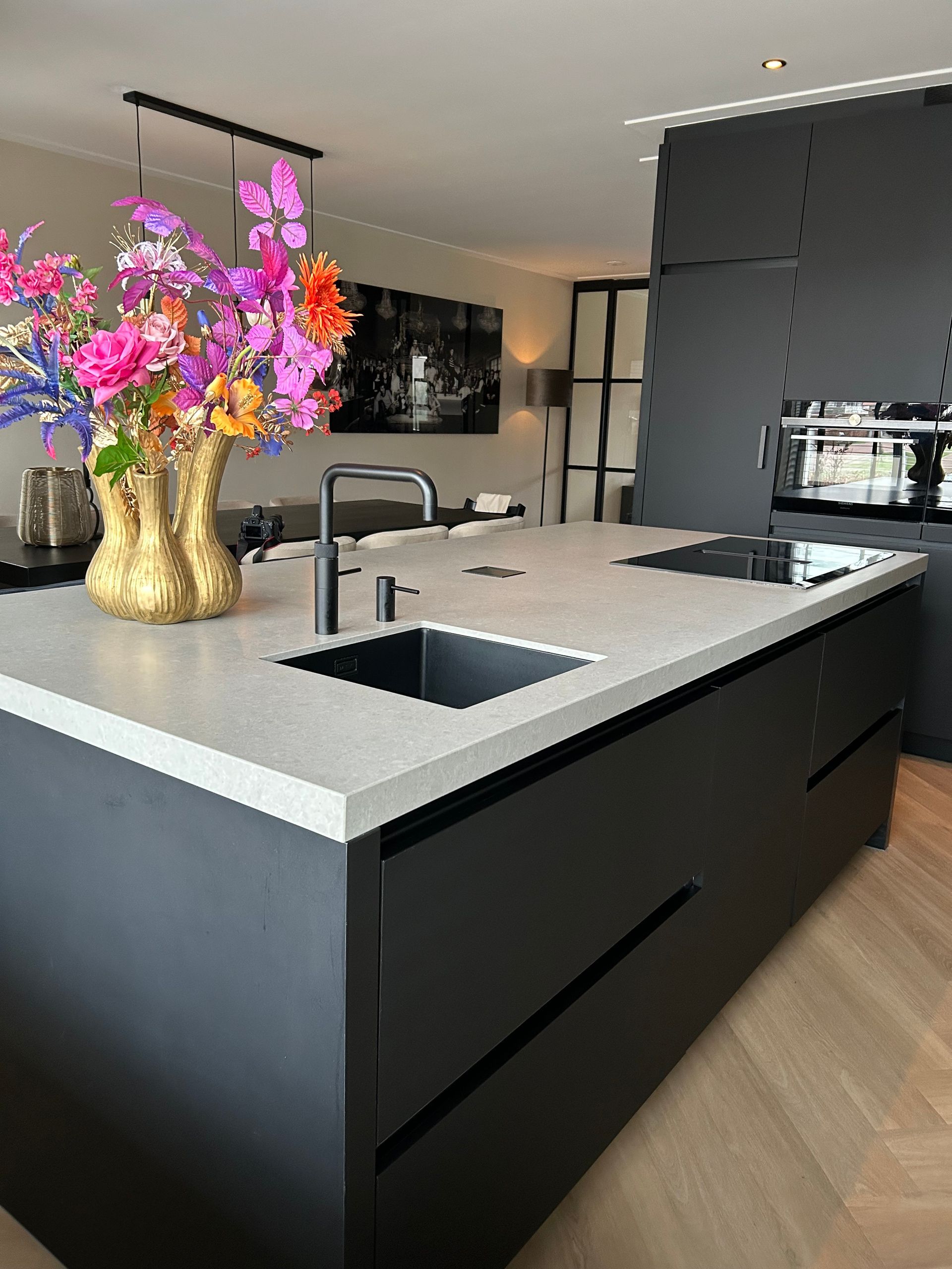 Moderne keuken met een zwart kookeiland, wit aanrechtblad, gouden vaas met roze bloemen en ingebouwde spoelbak.