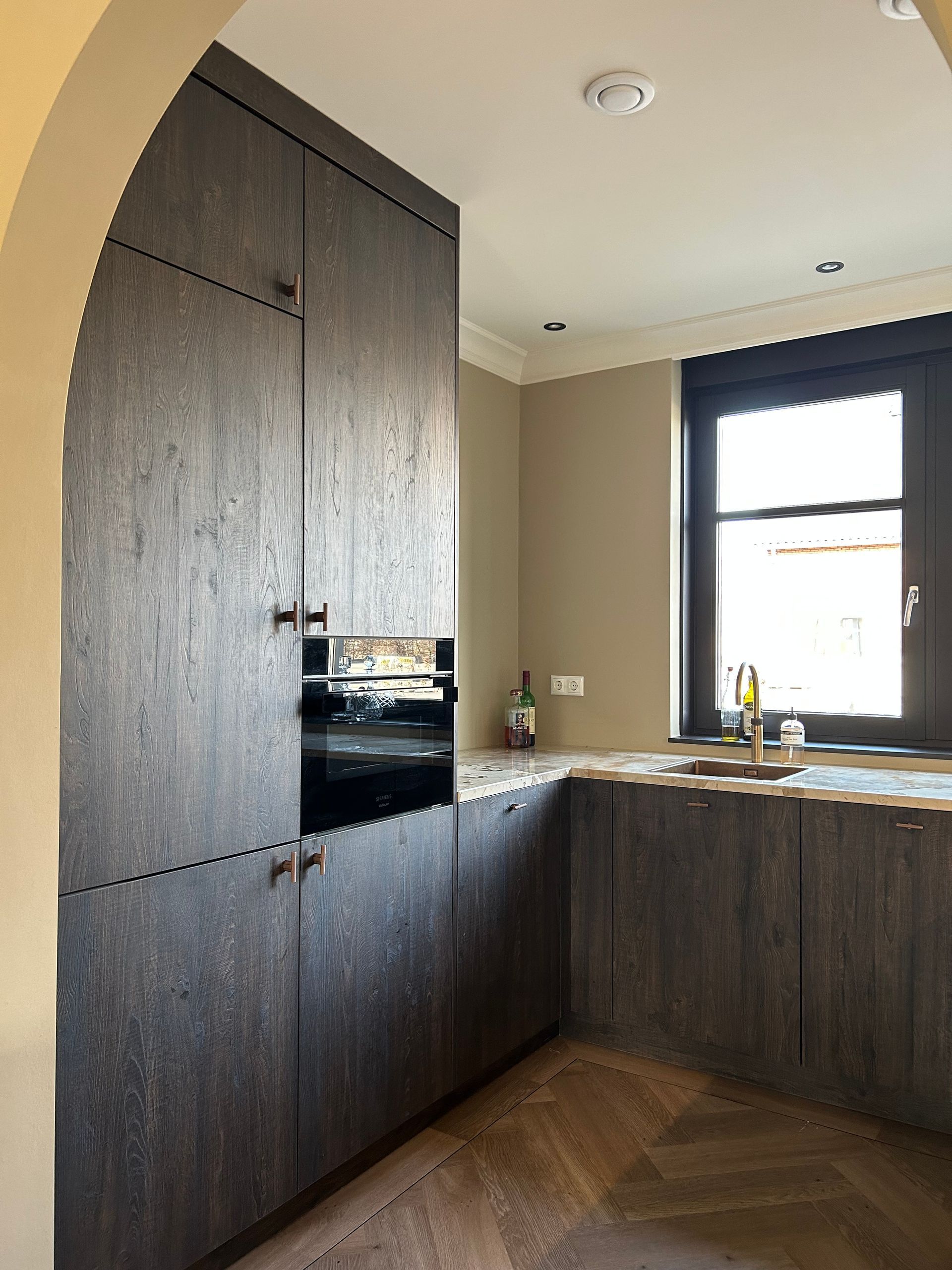 Moderne keuken met donkerhouten kasten, zwarte werkbladen en een raam boven de spoelbak.
