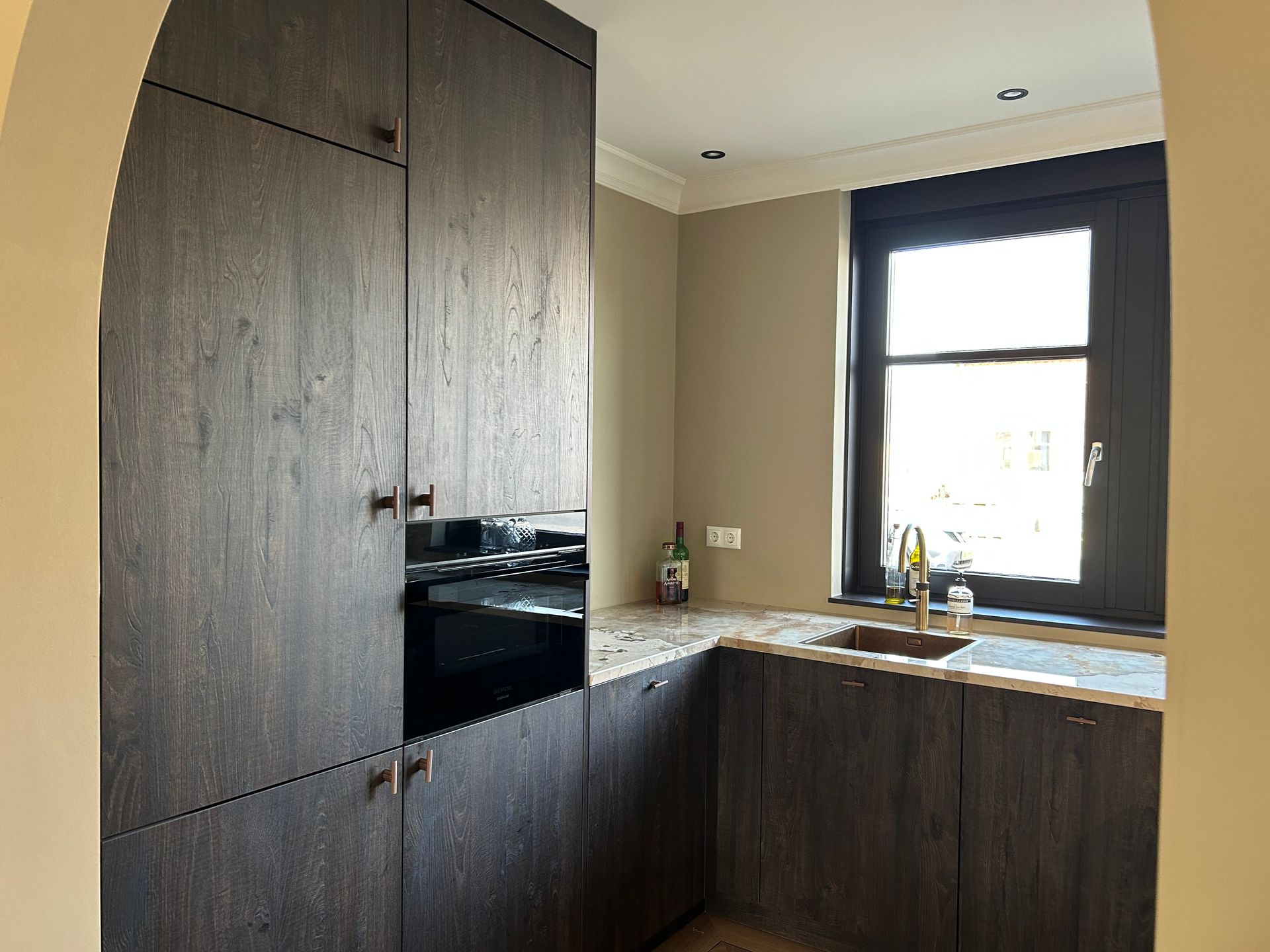 Moderne keuken met donkerhouten kasten, zwarte werkbladen en een raam boven de spoelbak.