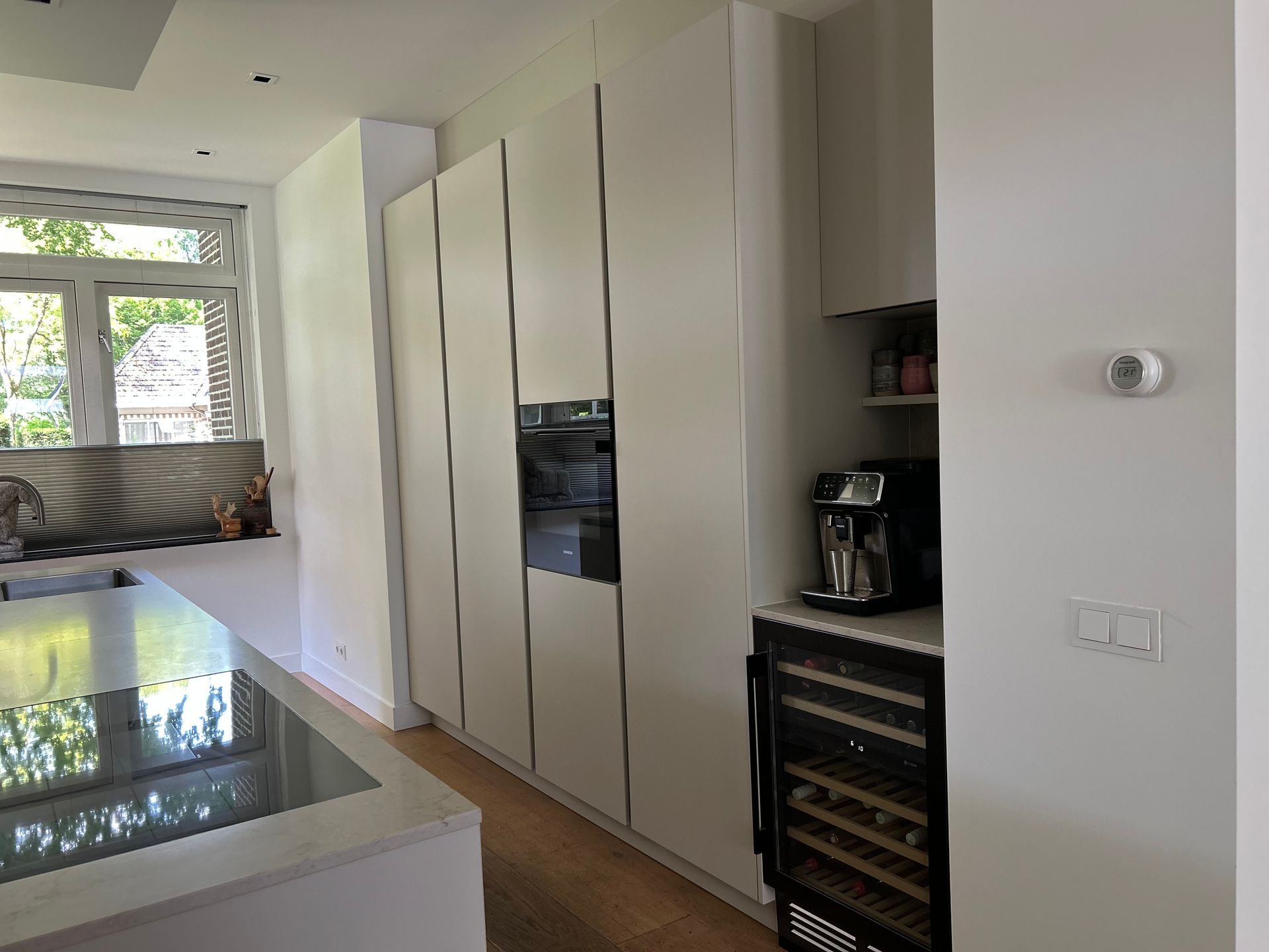 Moderne keuken met witte kasten, kookeiland, ingebouwde oven en koffiezetapparaat langs de muur.