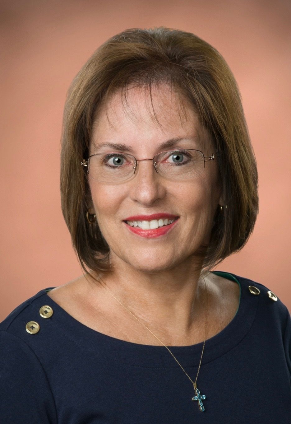 Woman with short brown hair, glasses, and a blue shirt, smiling and looking at the viewer.
