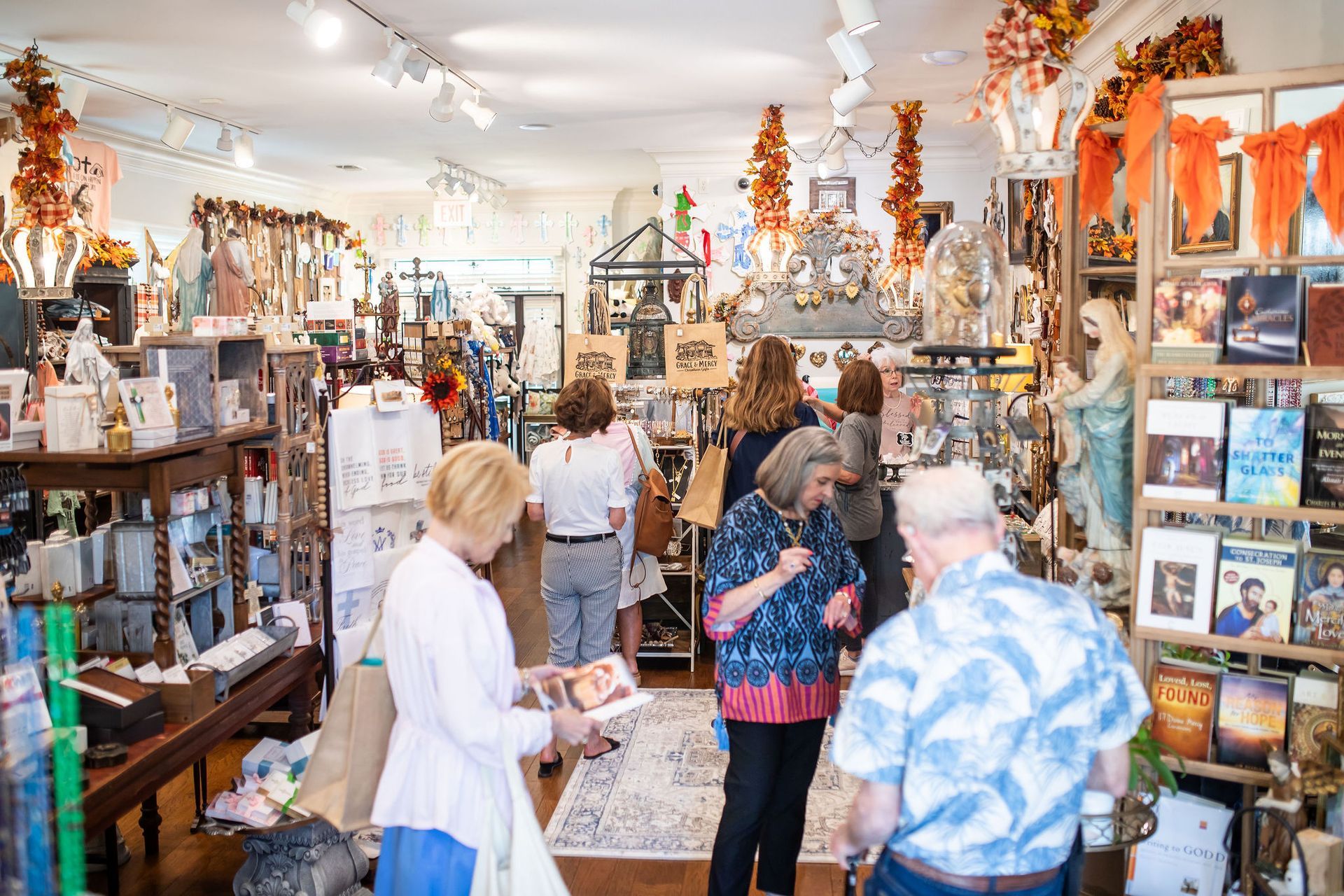 People browsing a brightly lit gift shop filled with decor, books, and flowers.