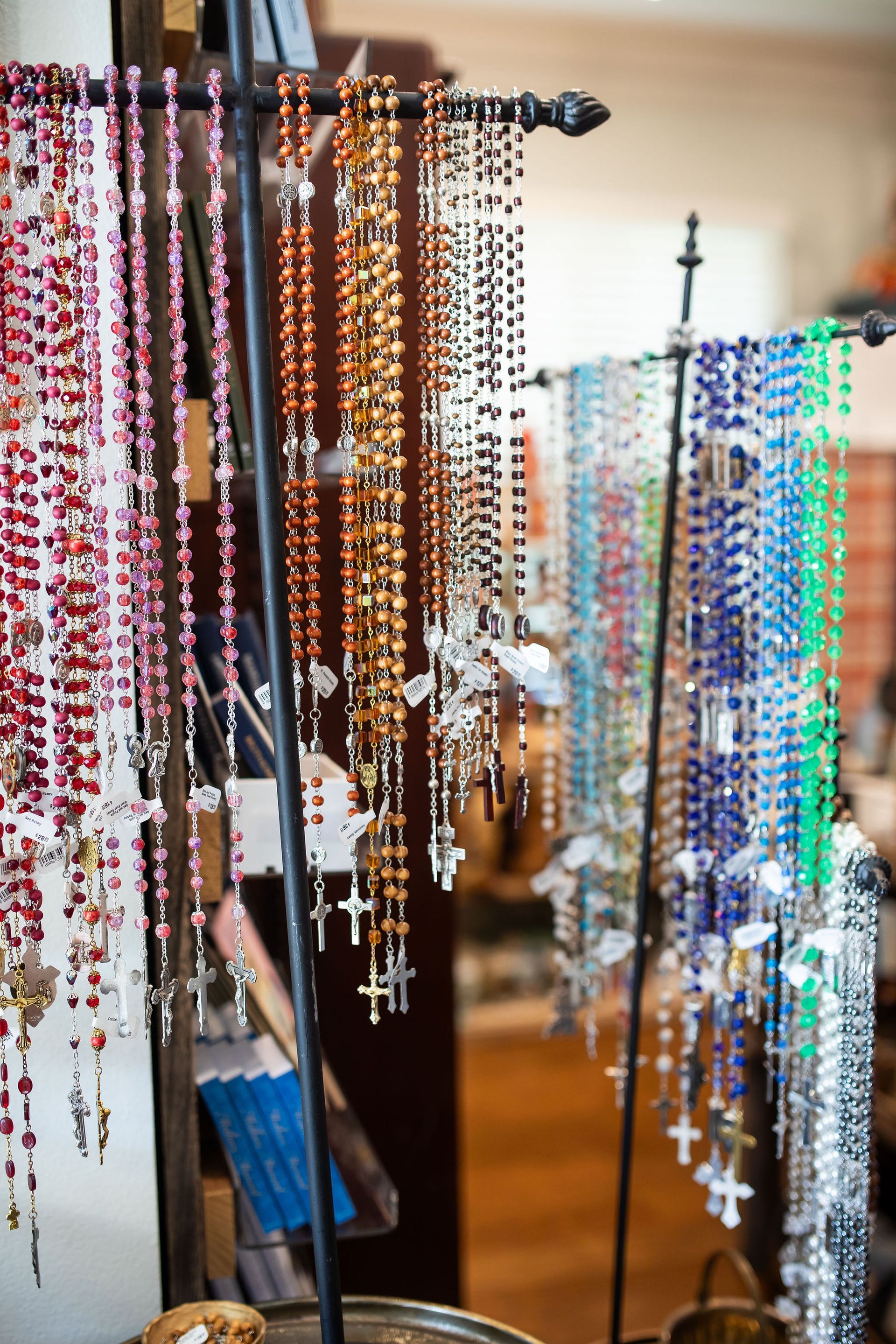 Rows of colorful rosaries hanging from a rack, each with a cross pendant.