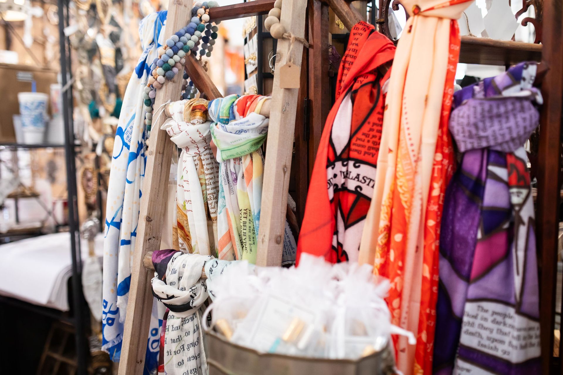 Scarves of various colors and patterns displayed on a wooden rack at a market.
