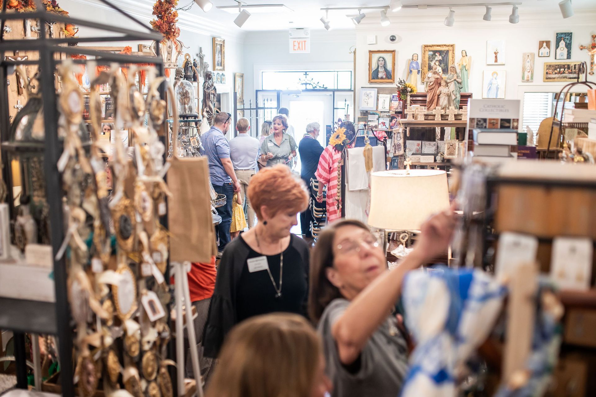 People browse merchandise in a crowded shop filled with items, including wall hangings and jewelry.