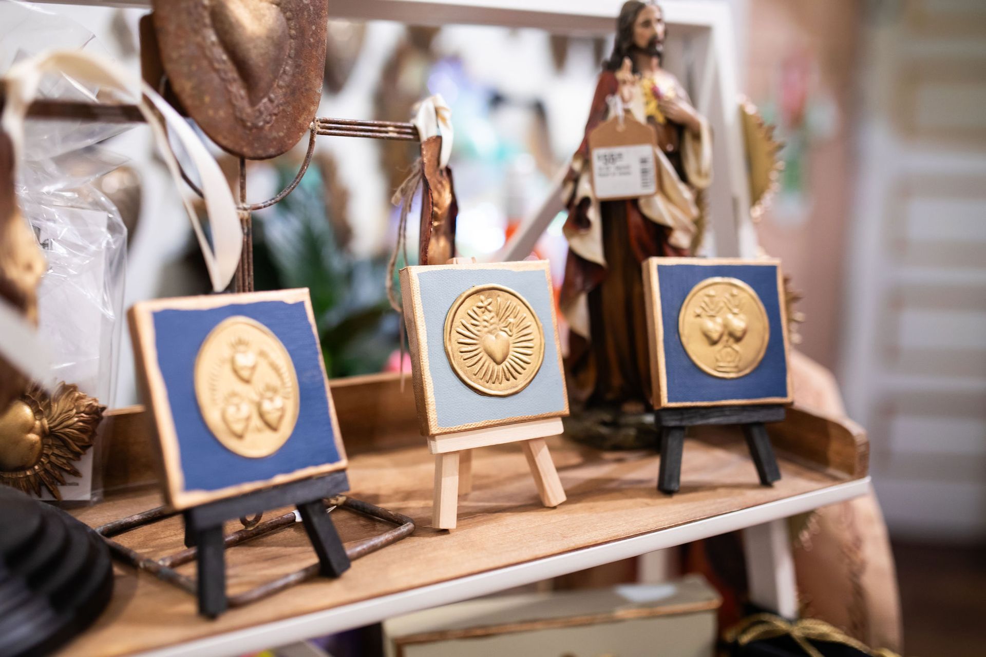 Three small framed medallions on miniature easels on a shelf, with a religious figurine in the background.