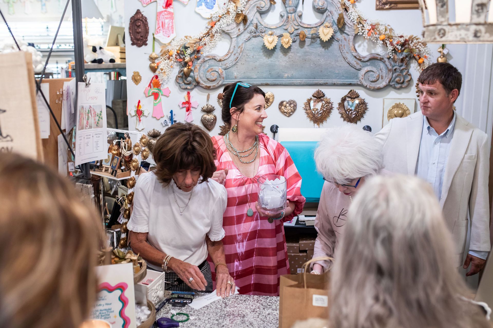 People shopping in a shop filled with trinkets. Woman in pink shirt smiles, others browse items.
