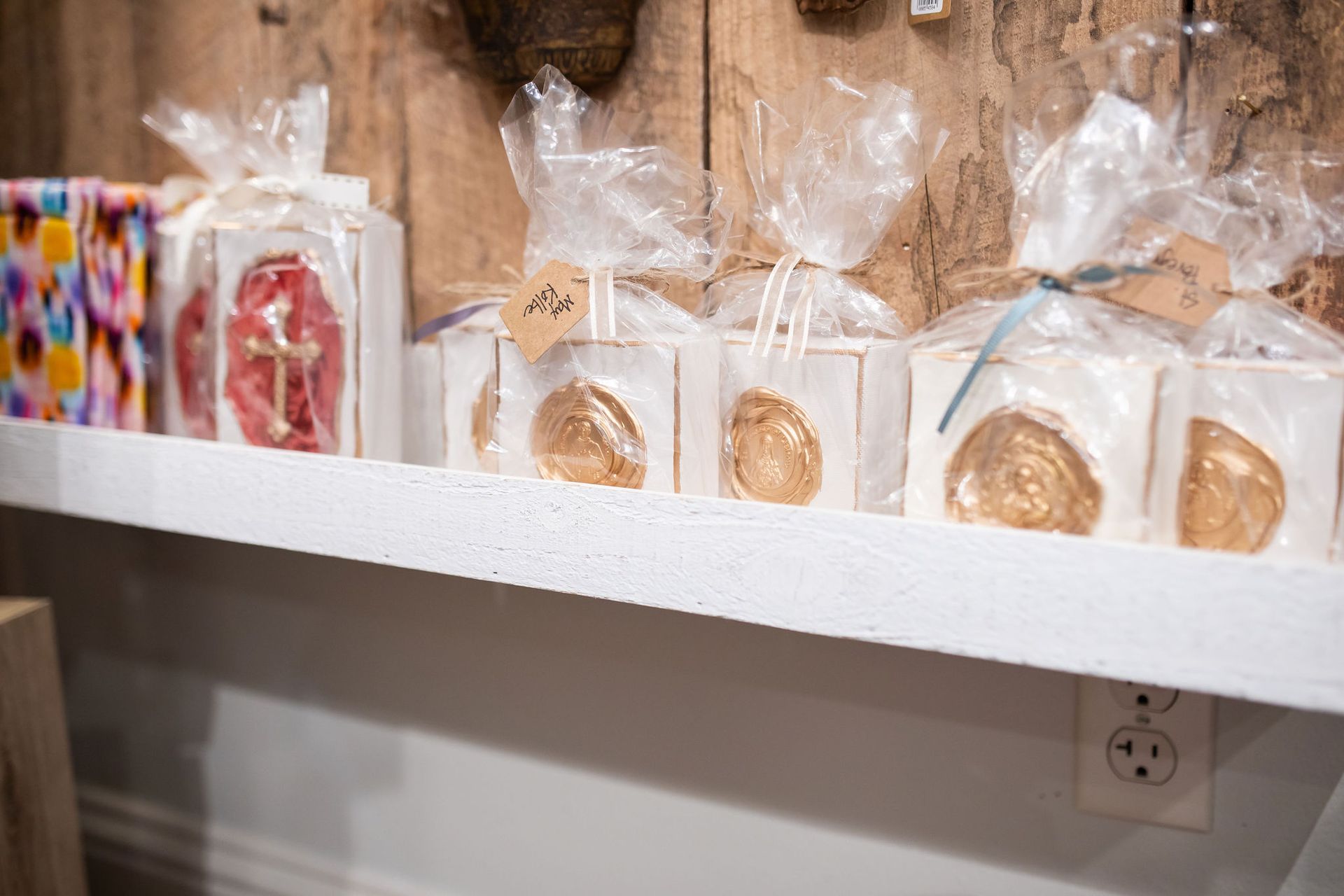 Shelf displaying wrapped items, including gold-colored oyster shell decor and colorful patterned blocks against a wooden background.