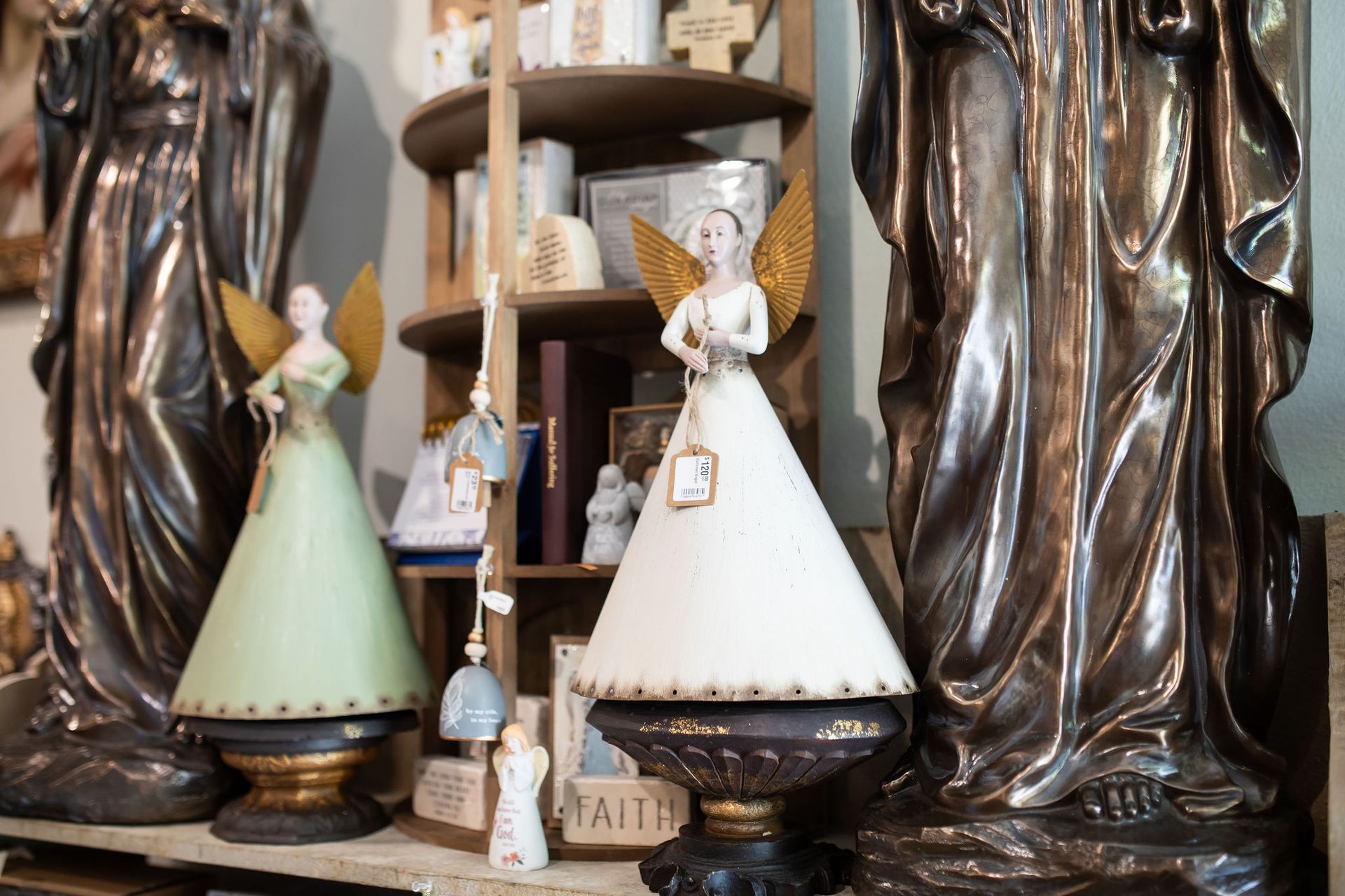 Two angel figurines with gold wings on display in a shop, flanked by statues.
