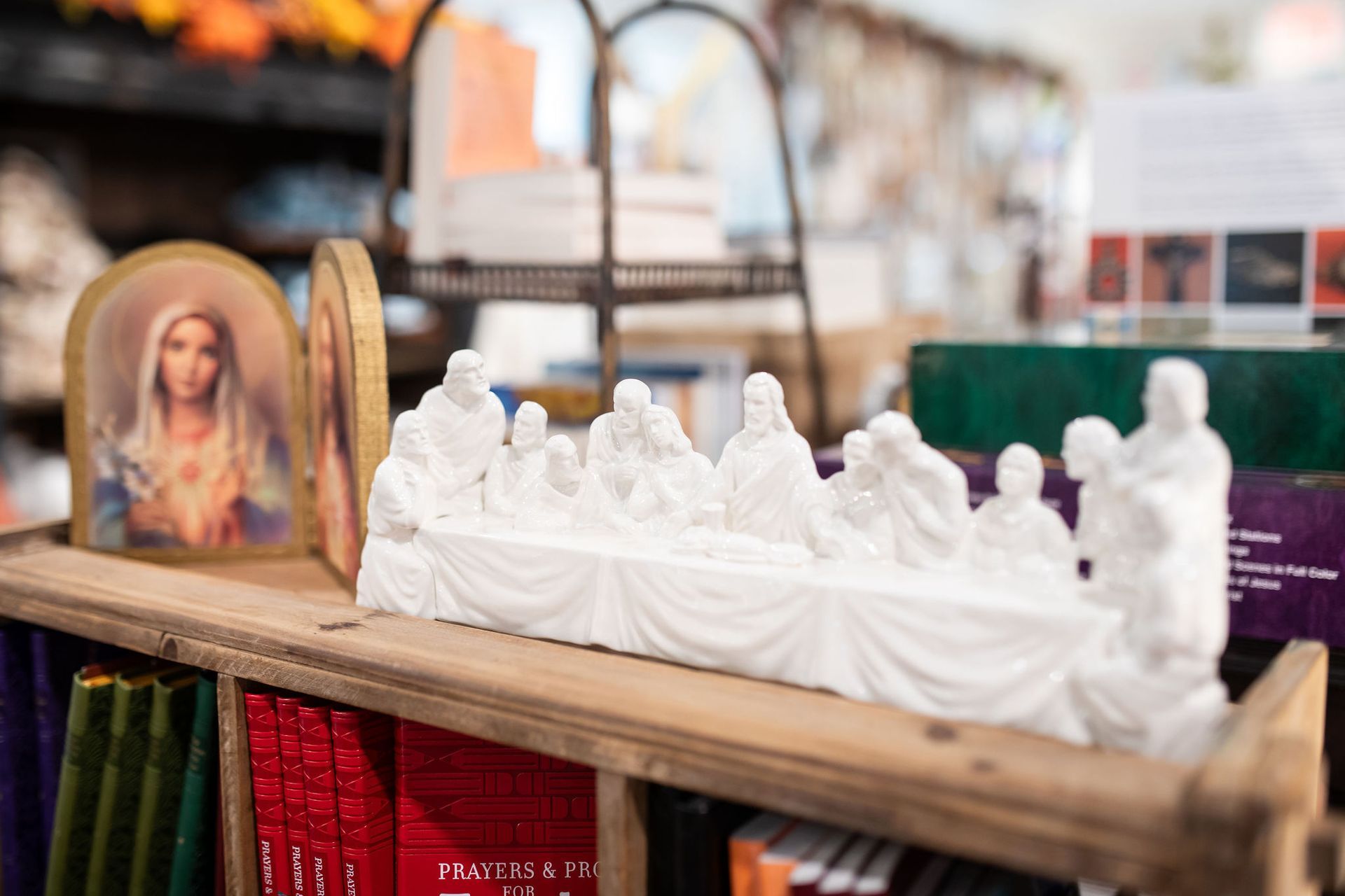 White plaster sculpture of the Last Supper, displayed on a wooden shelf with other religious items.