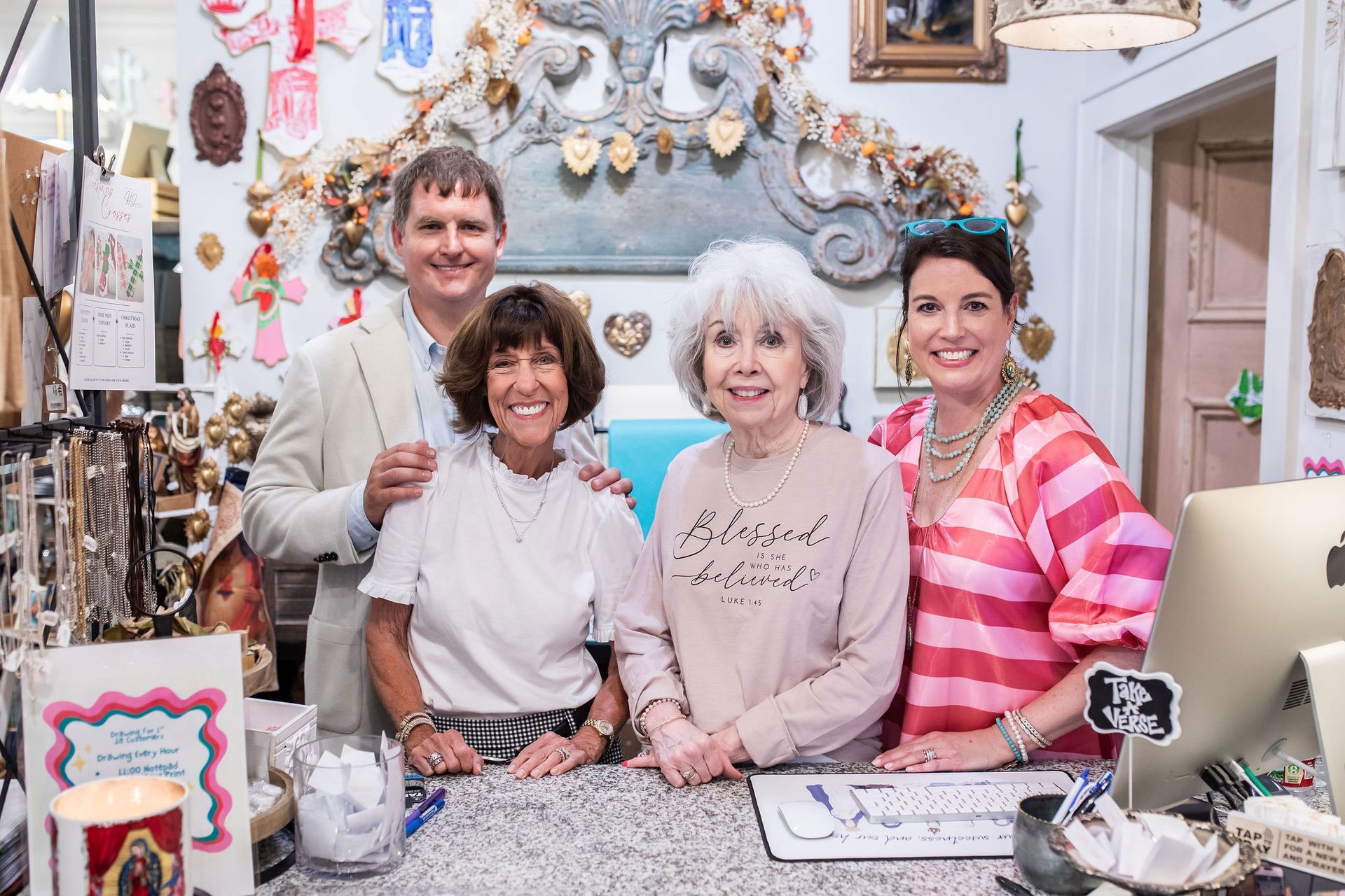Four people smiling at the camera behind a shop counter filled with merchandise.