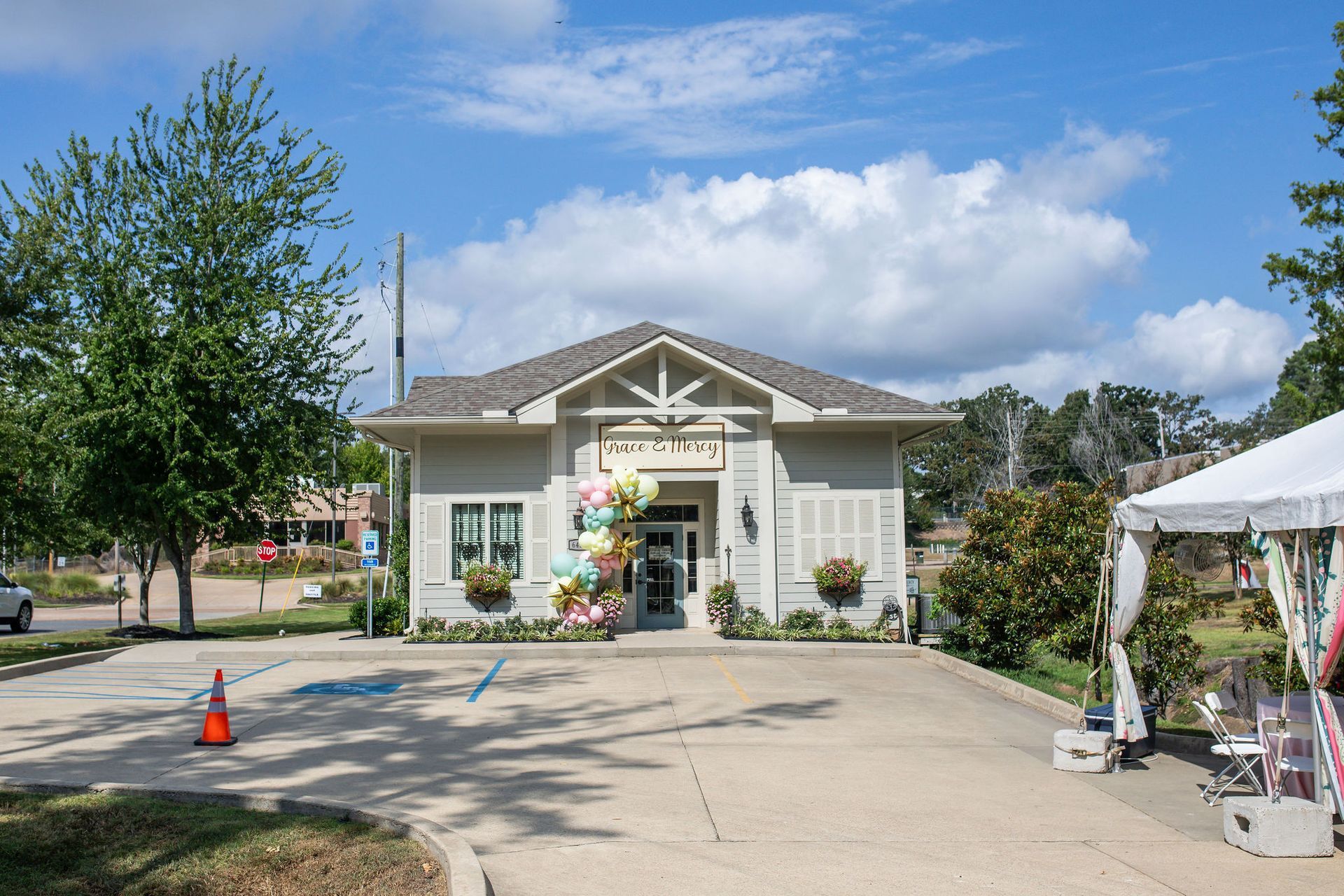 A light gray building with balloons, a tent, and a parking lot on a sunny day.