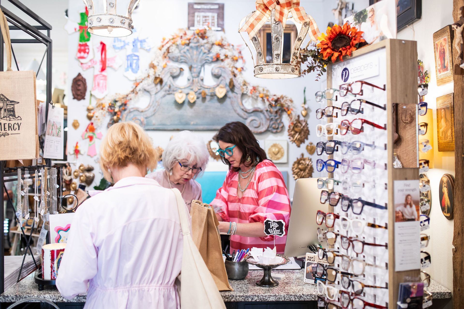 Three people examining items at an eyeglass shop counter. The interior is decorated with ornate objects.