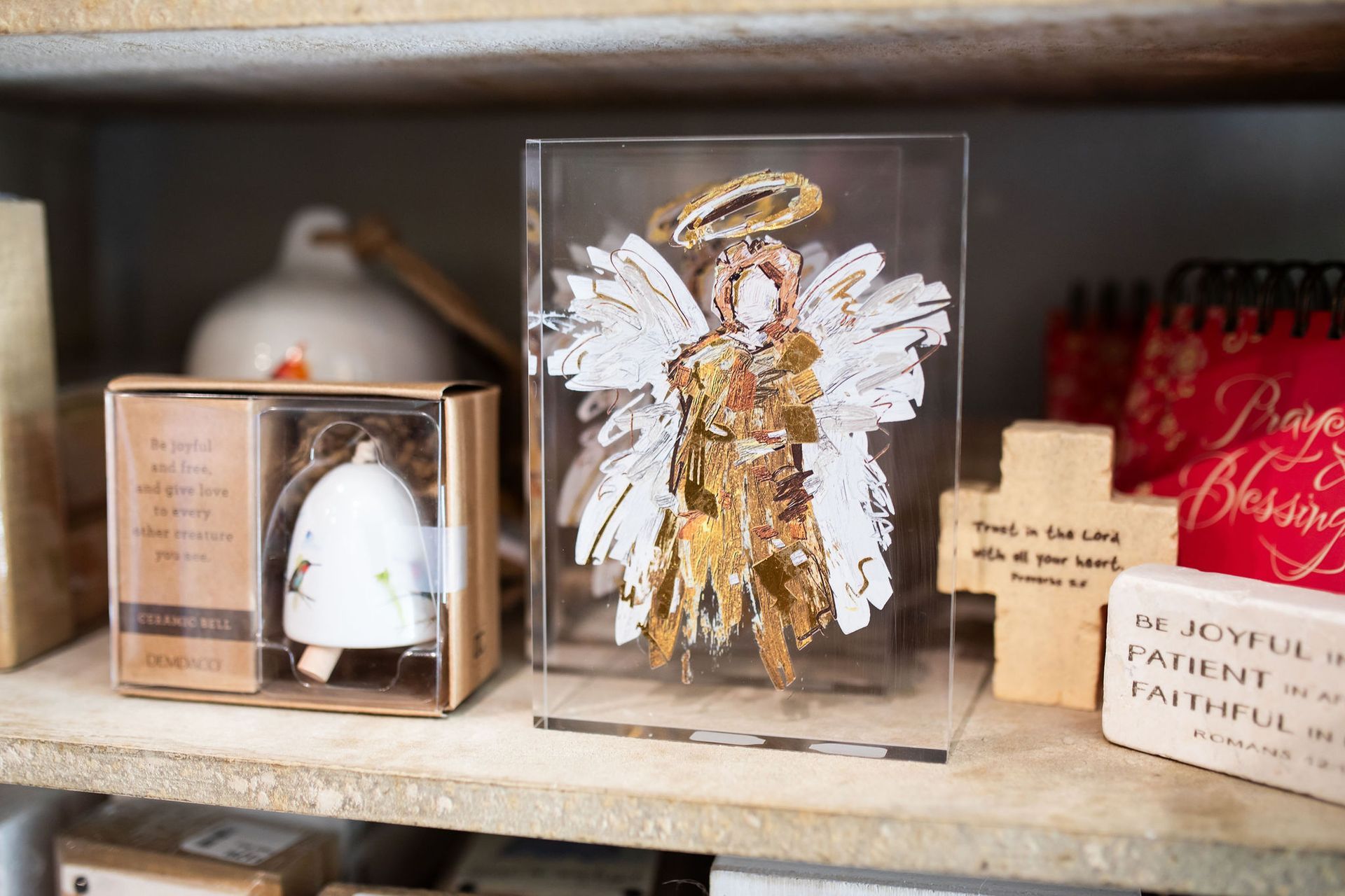 Shelf with angel figure, bell, wooden cross, and red decor.