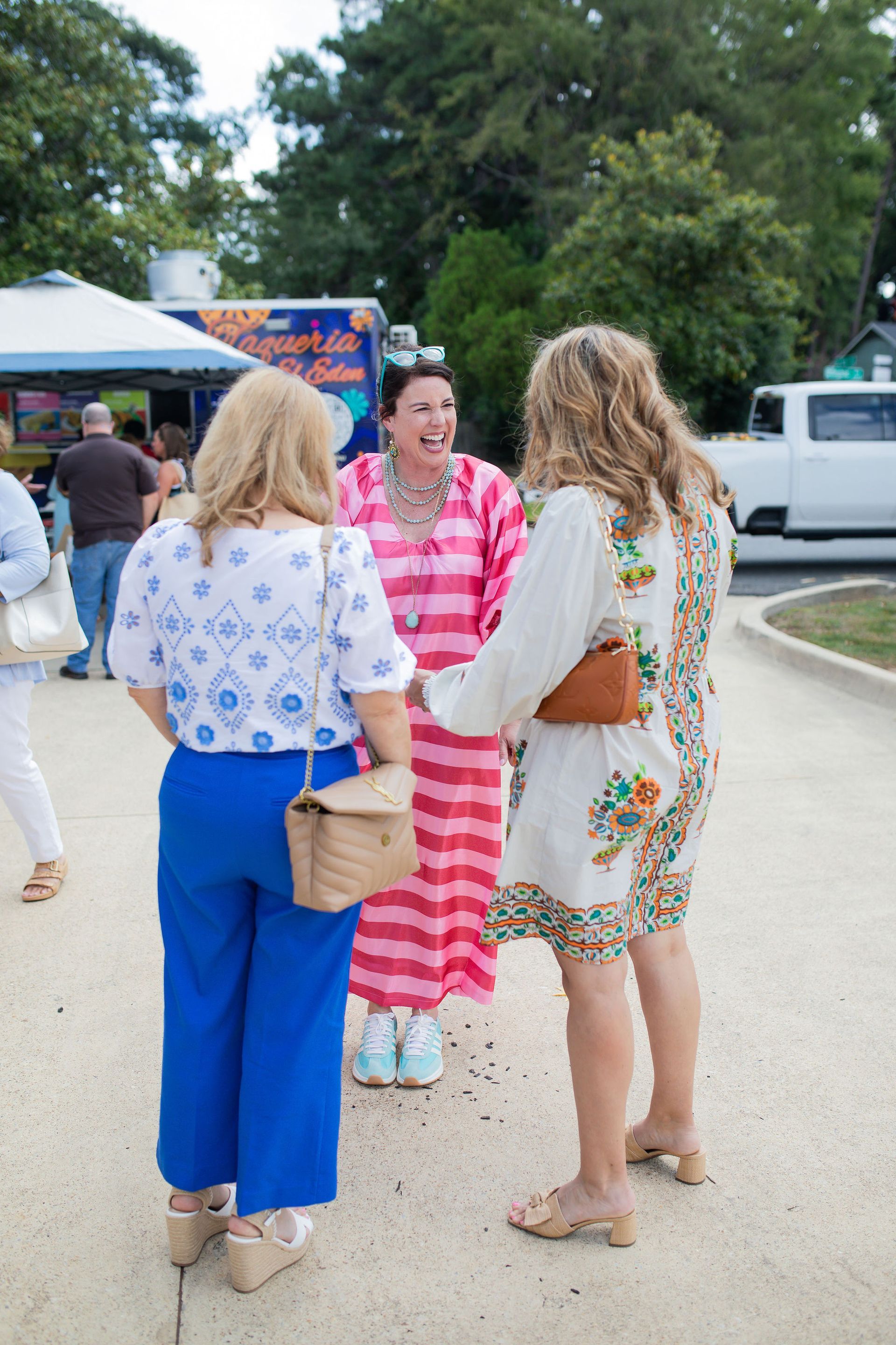Three women in colorful clothing converse outside; one in pink and white stripes, others in blue, white, and floral prints.