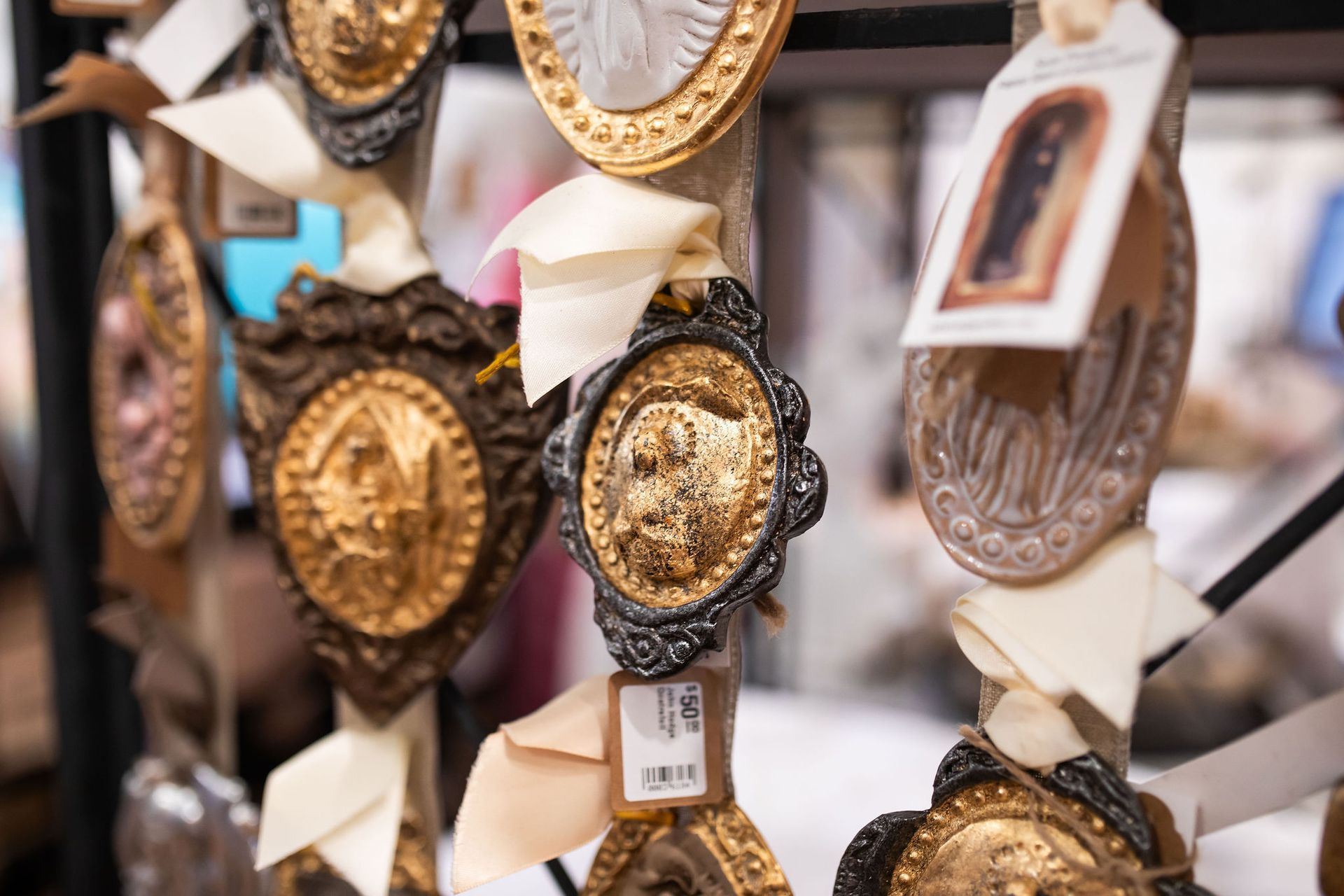 Ornate golden medallions with attached tags, hanging from a rack, a display of religious art.
