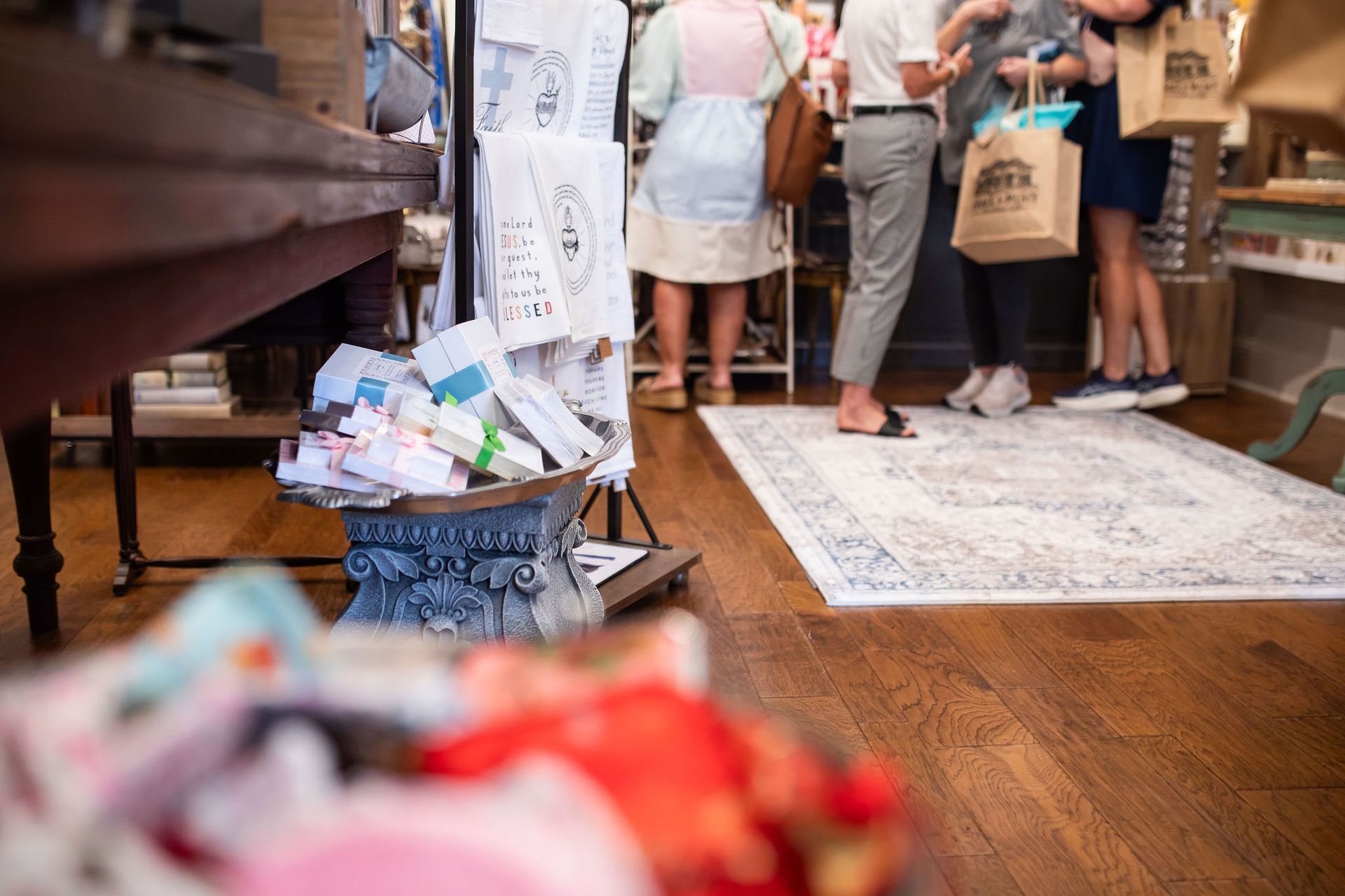 People shopping in a store. Wooden floors, a rug, and merchandise on display.