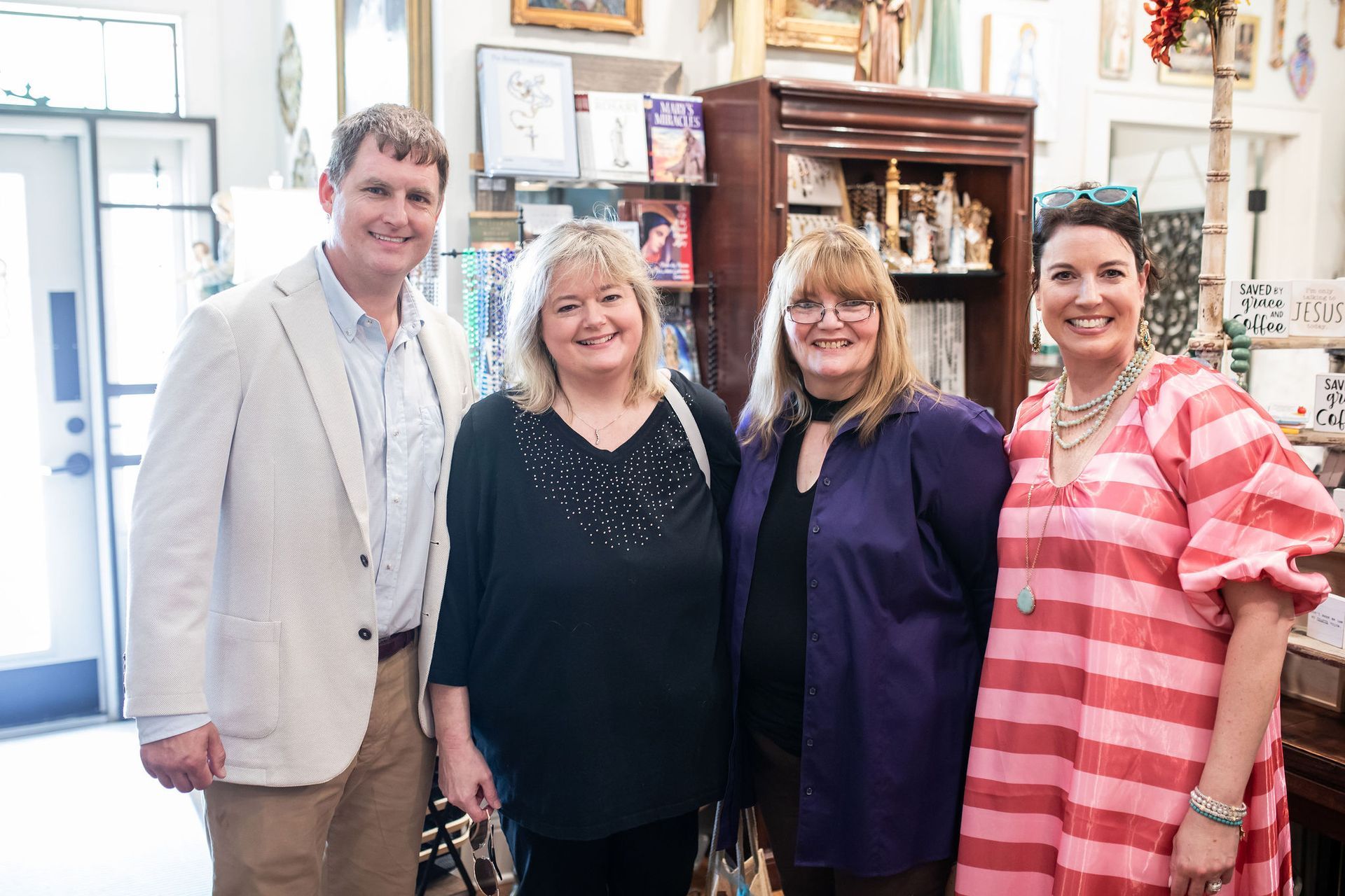 Four people posing in a shop, two women smiling. Shop is filled with art and items.