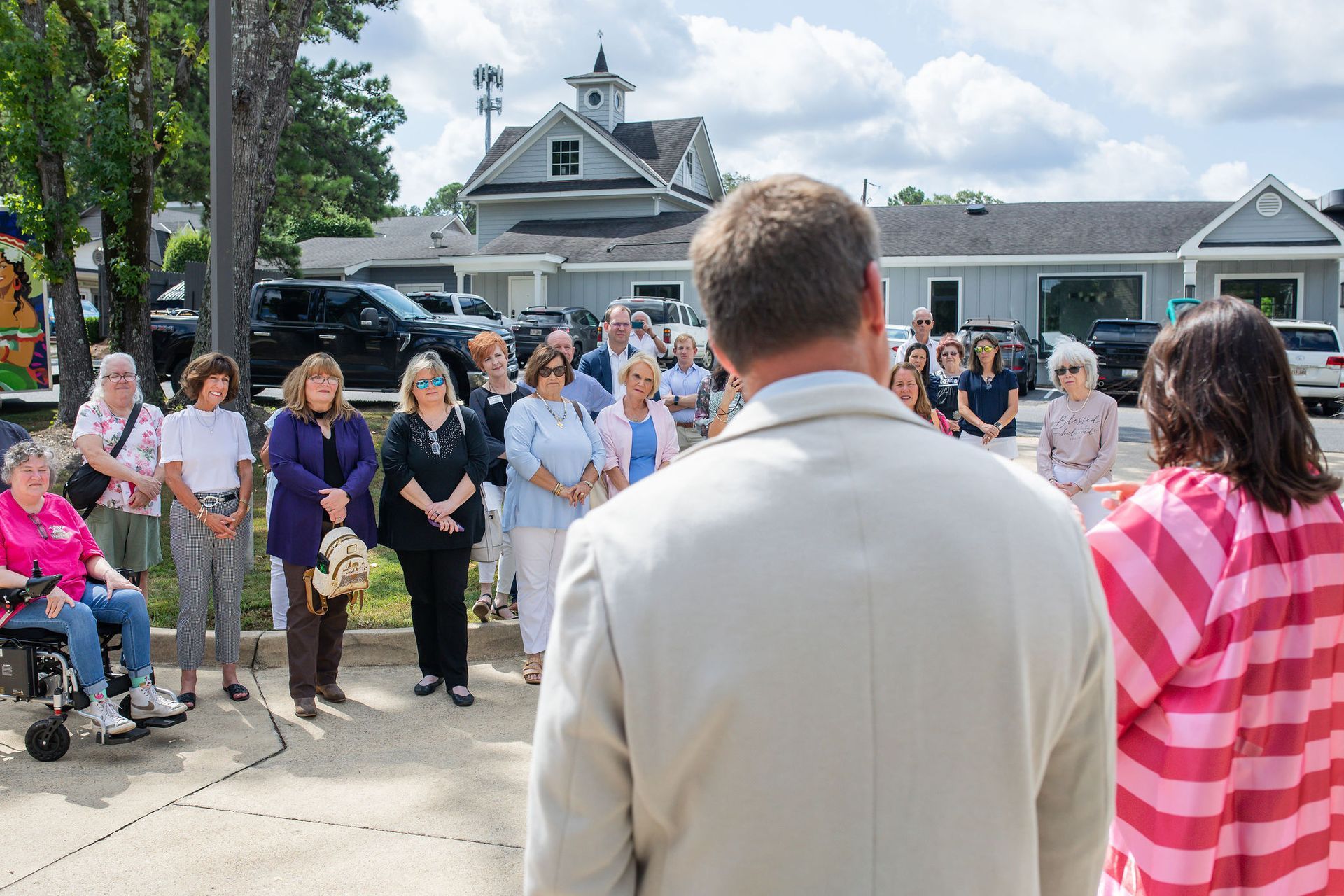 Group of people listening to two individuals speaking outdoors, in front of buildings.