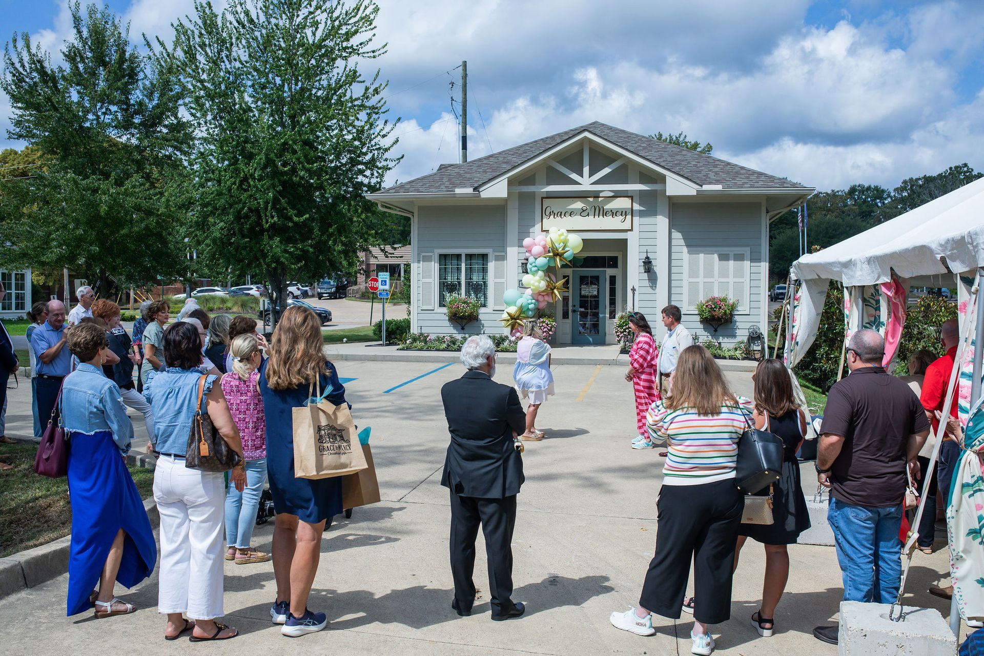 People gather outside a small building with balloons, under a bright sky.