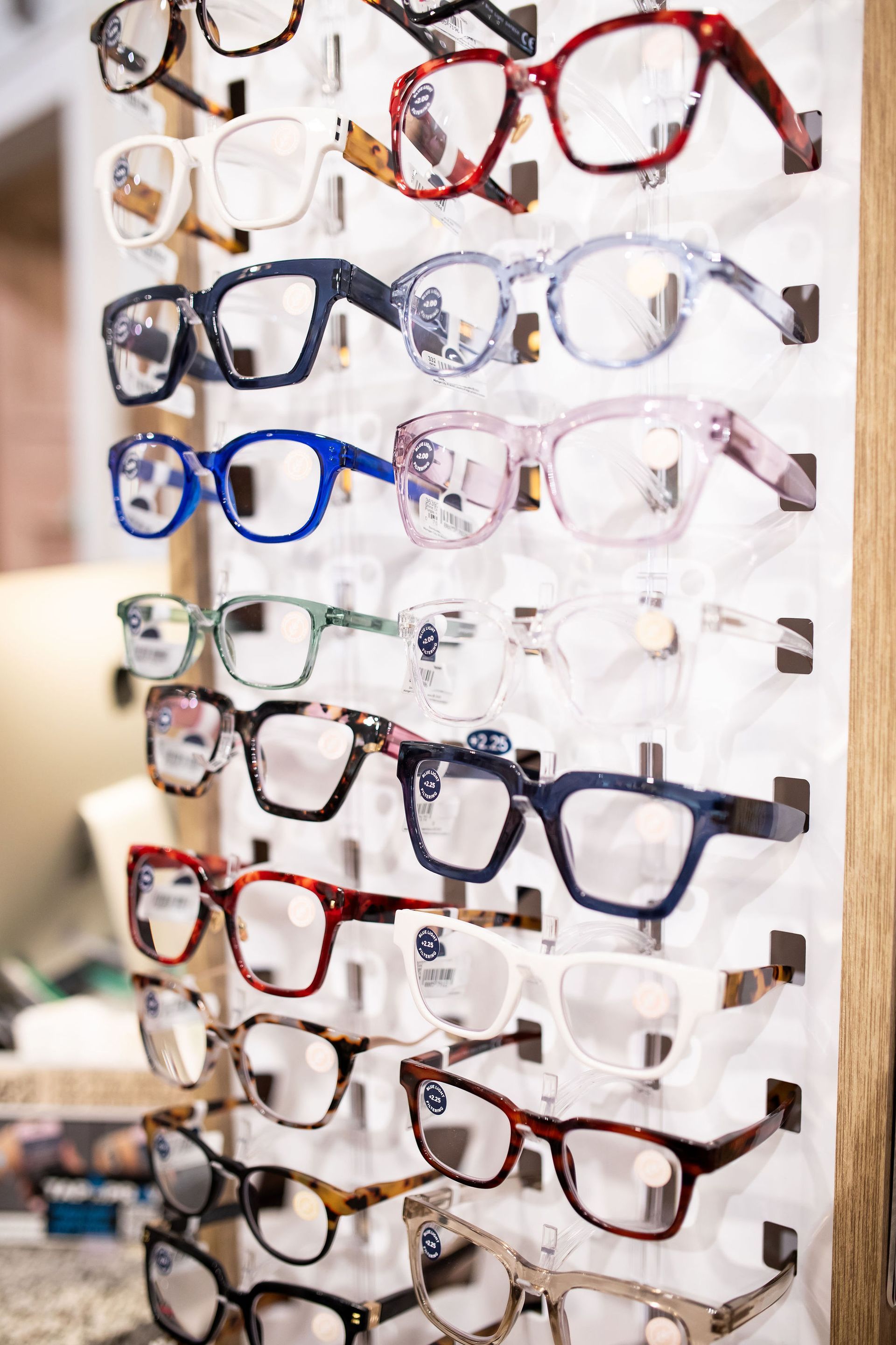 Eyeglass frames displayed on a pegboard in a shop, with various colors and styles.