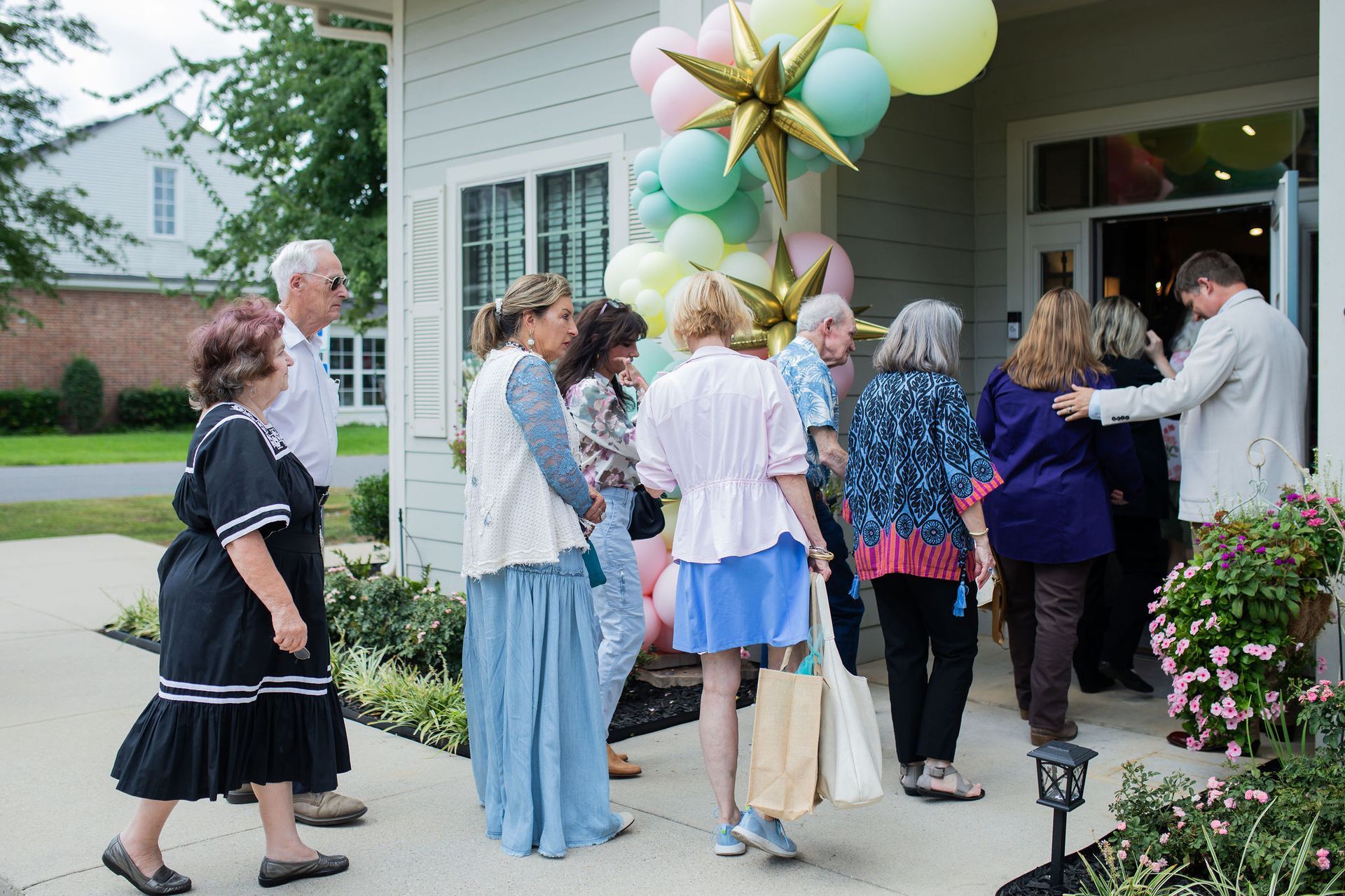 People entering a building with pastel balloons. A man holds the door open for the group.