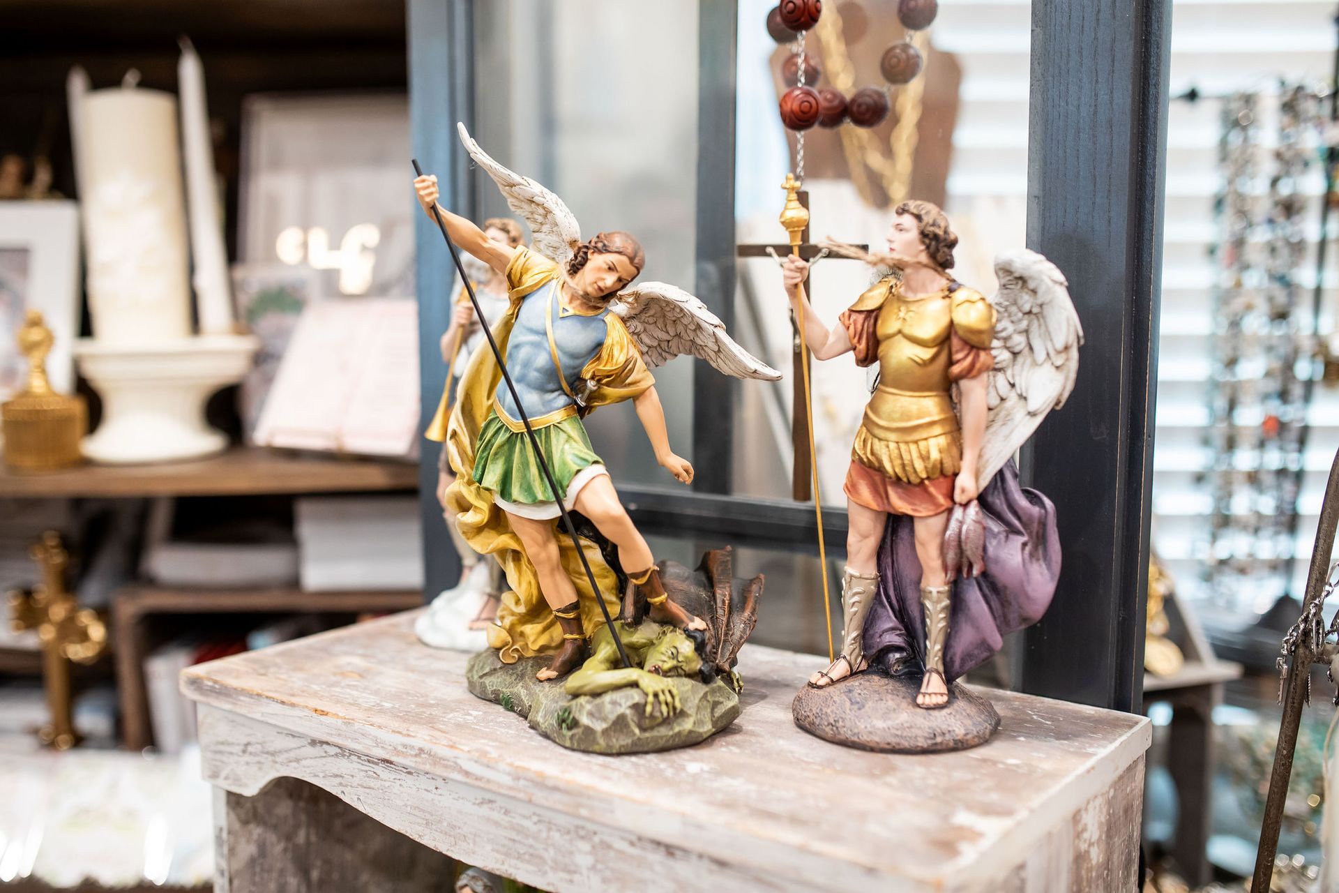 Two angel figurines with wings, in a shop setting. One raises a spear, the other holds a staff.