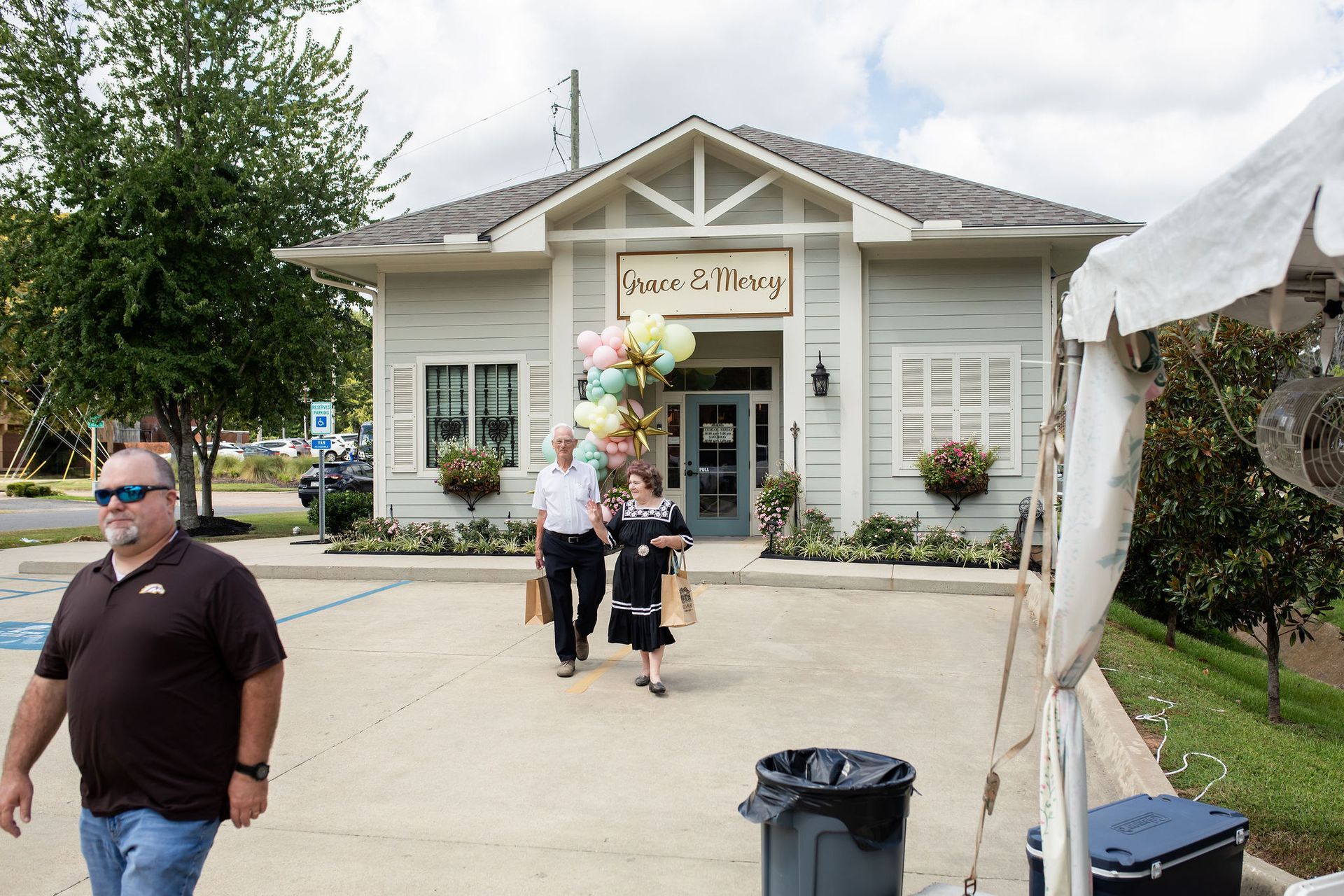 People exit a store, carrying bags. Pastel balloons near the door. Store sign says 