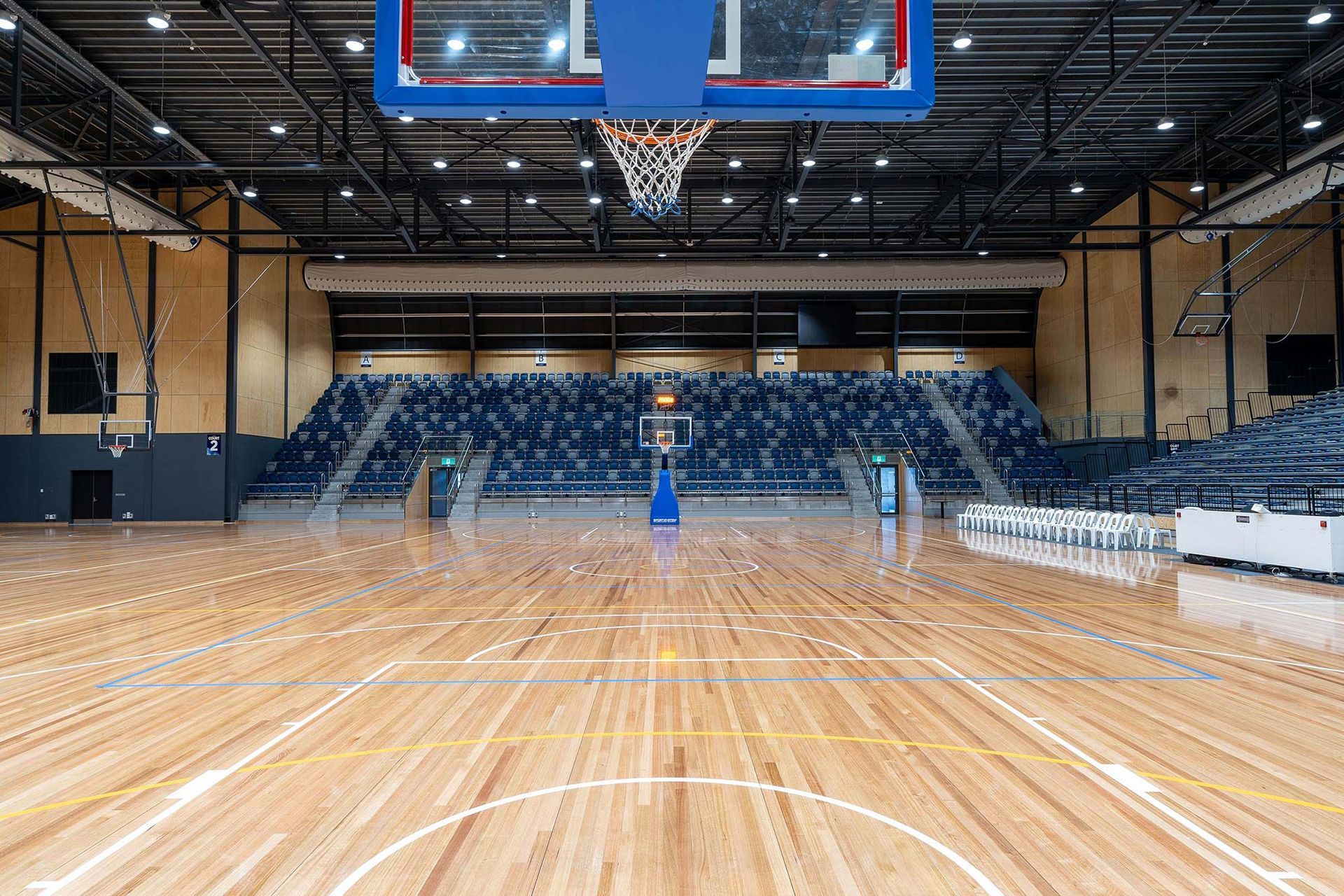 An empty basketball court with a wooden floor and a basketball hoop.