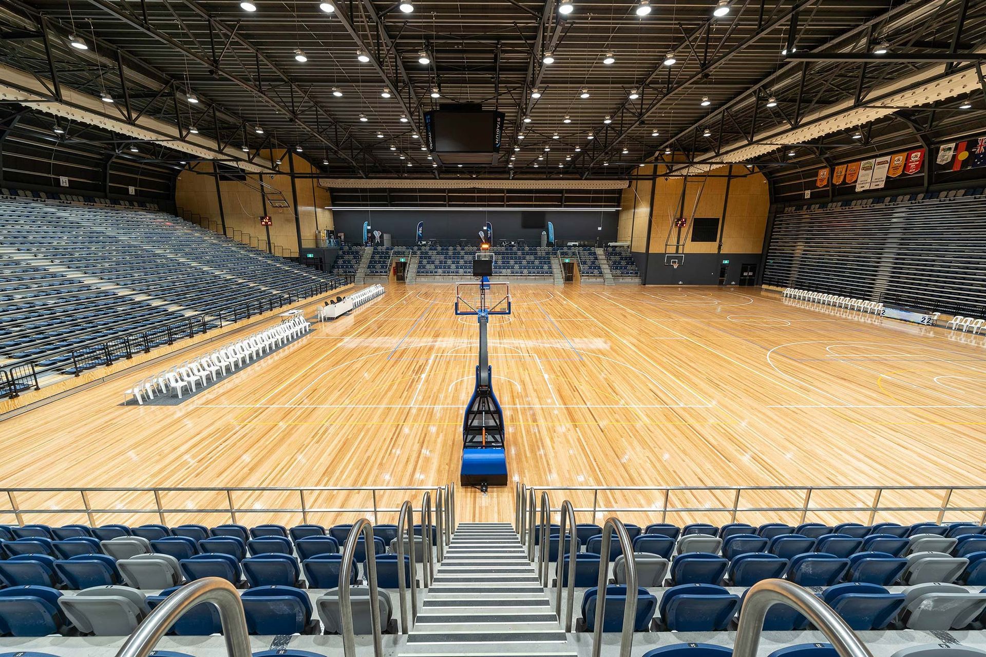 An empty basketball court in a large stadium with stairs leading up to it.
