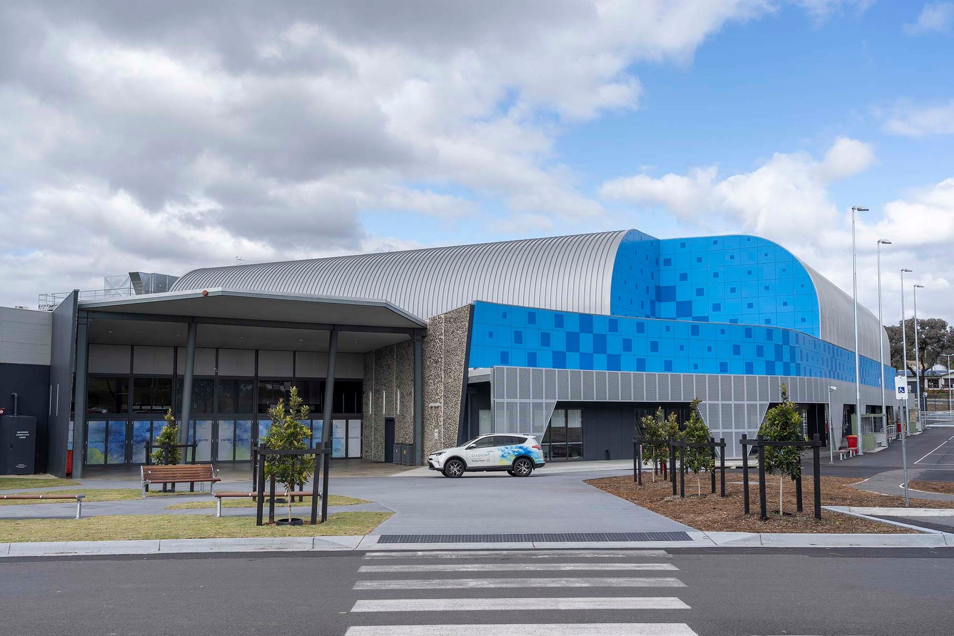 A white car is parked in front of a large blue building.