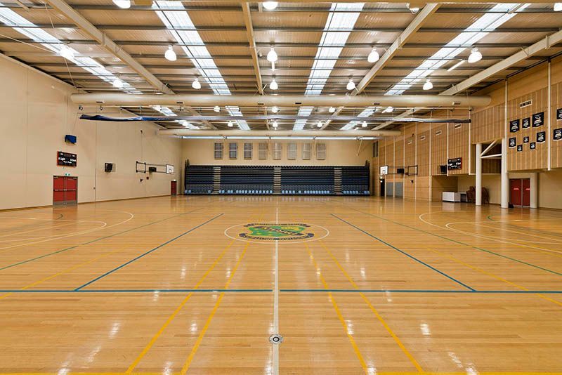 A large empty gym with a wooden floor and bleachers.