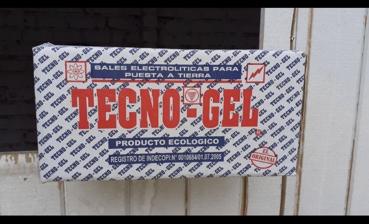 Caja de producto TECNO-GEL con letras rojas sobre fondo blanco, colocada contra una pared.
