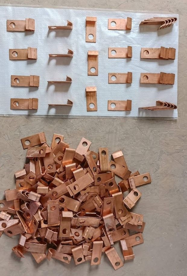 Pinzas metálicas de color cobre dispuestas sobre una pizarra blanca, con una pila de las mismas pinzas debajo.