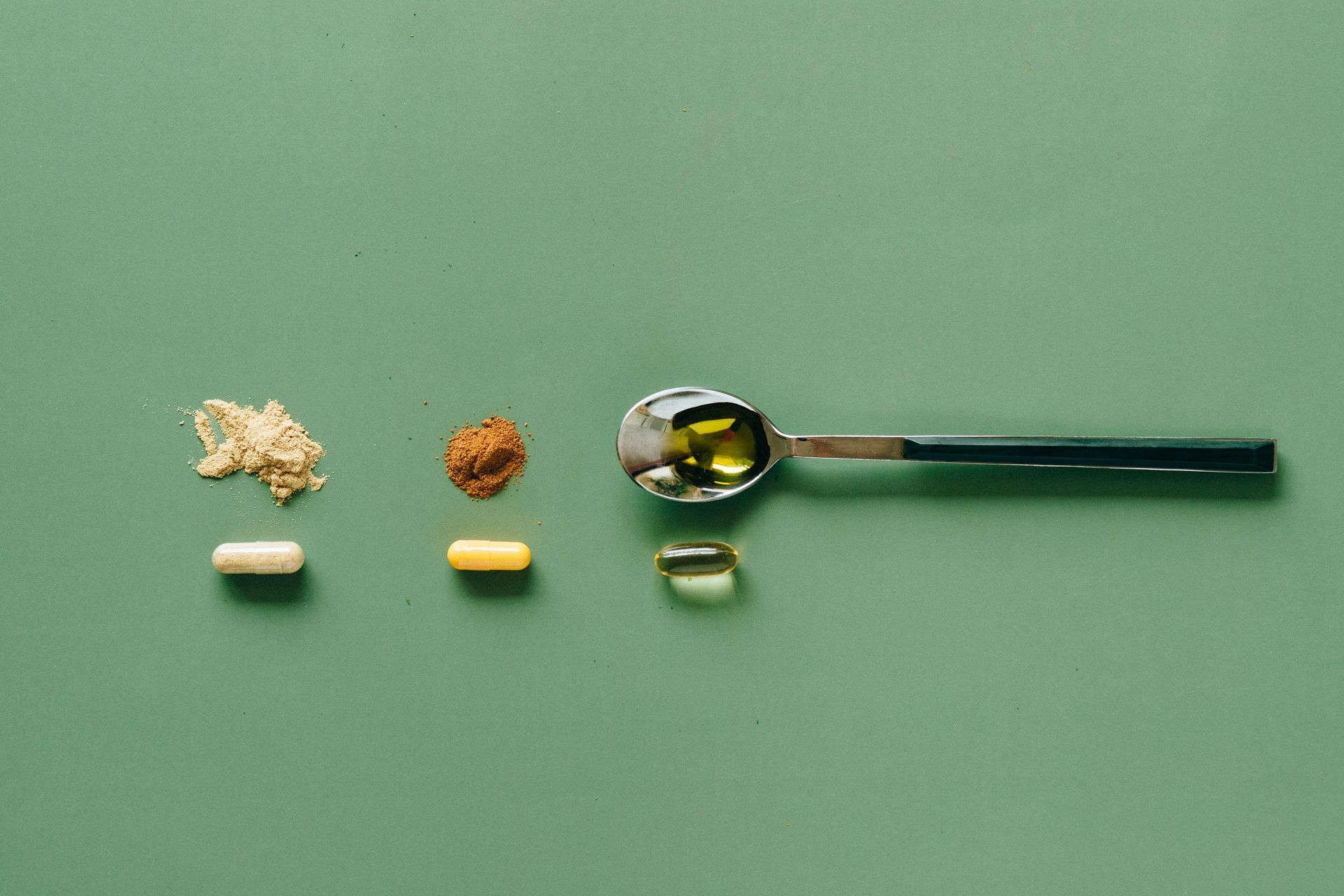 Supplements and powders arranged on a green surface with a spoon of liquid.