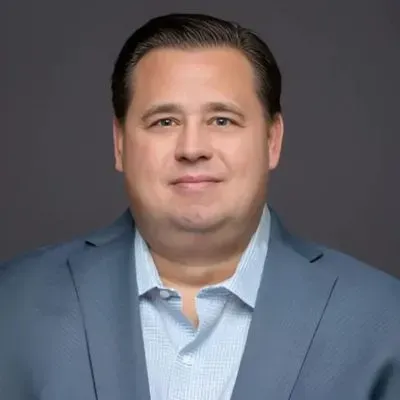 Studio portrait of a man in a blue blazer and light striped shirt against a gray background